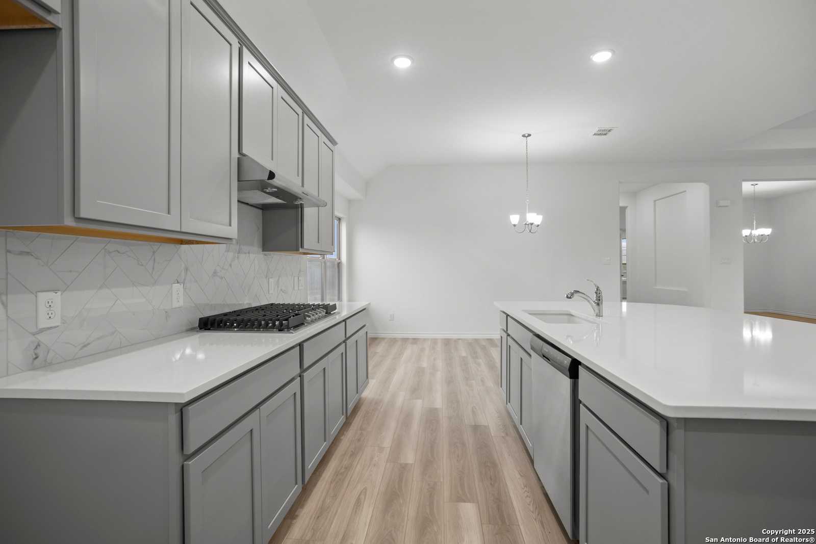 Modern open-concept kitchen with gray shaker cabinets, white quartz counters, and geometric tile backsplash in Davidson Homes The Summerlin B, Castroville, TX