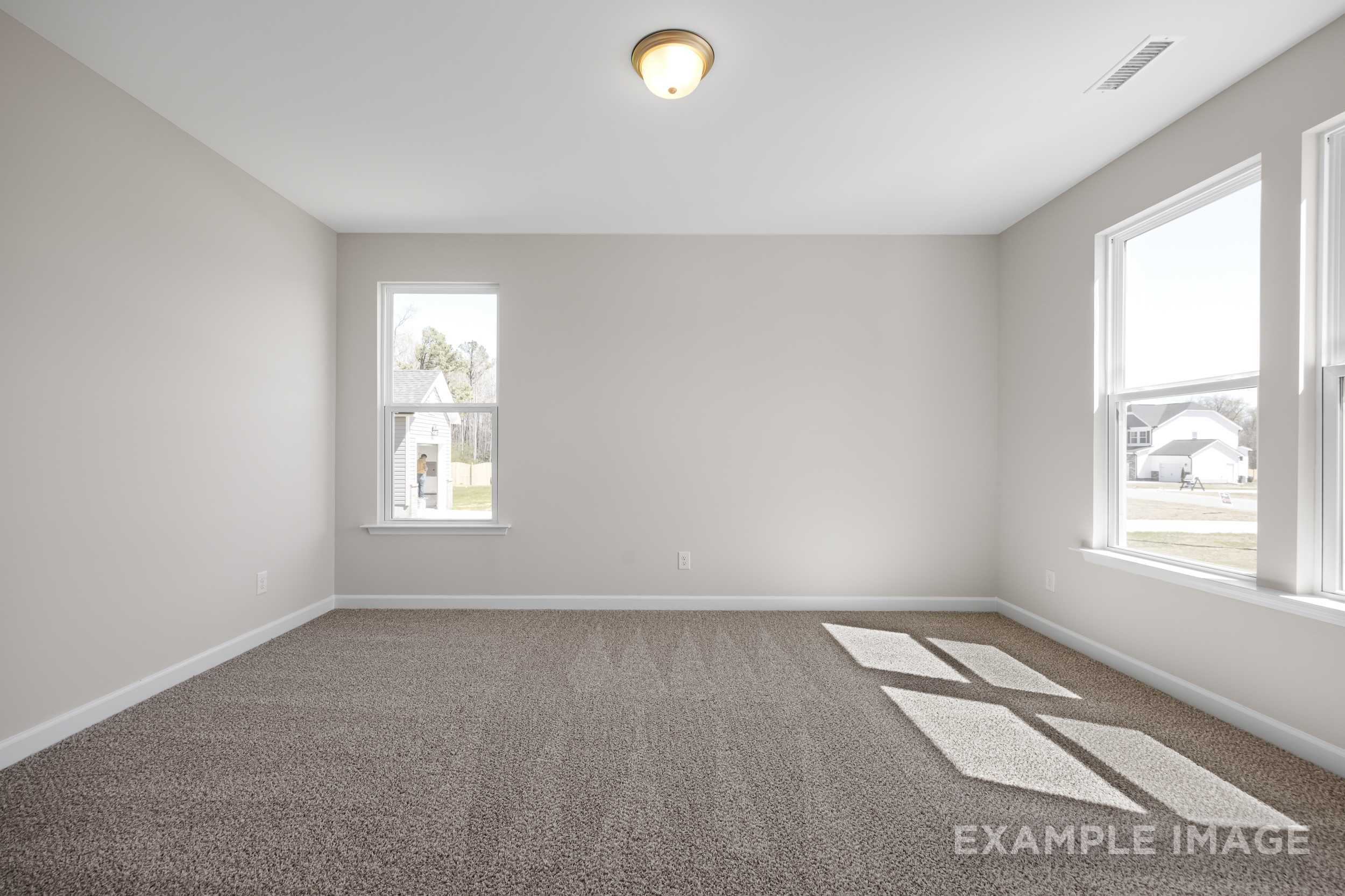 Spacious empty master bedroom in The Hickory II with beige walls, large windows, natural light, and brown carpet