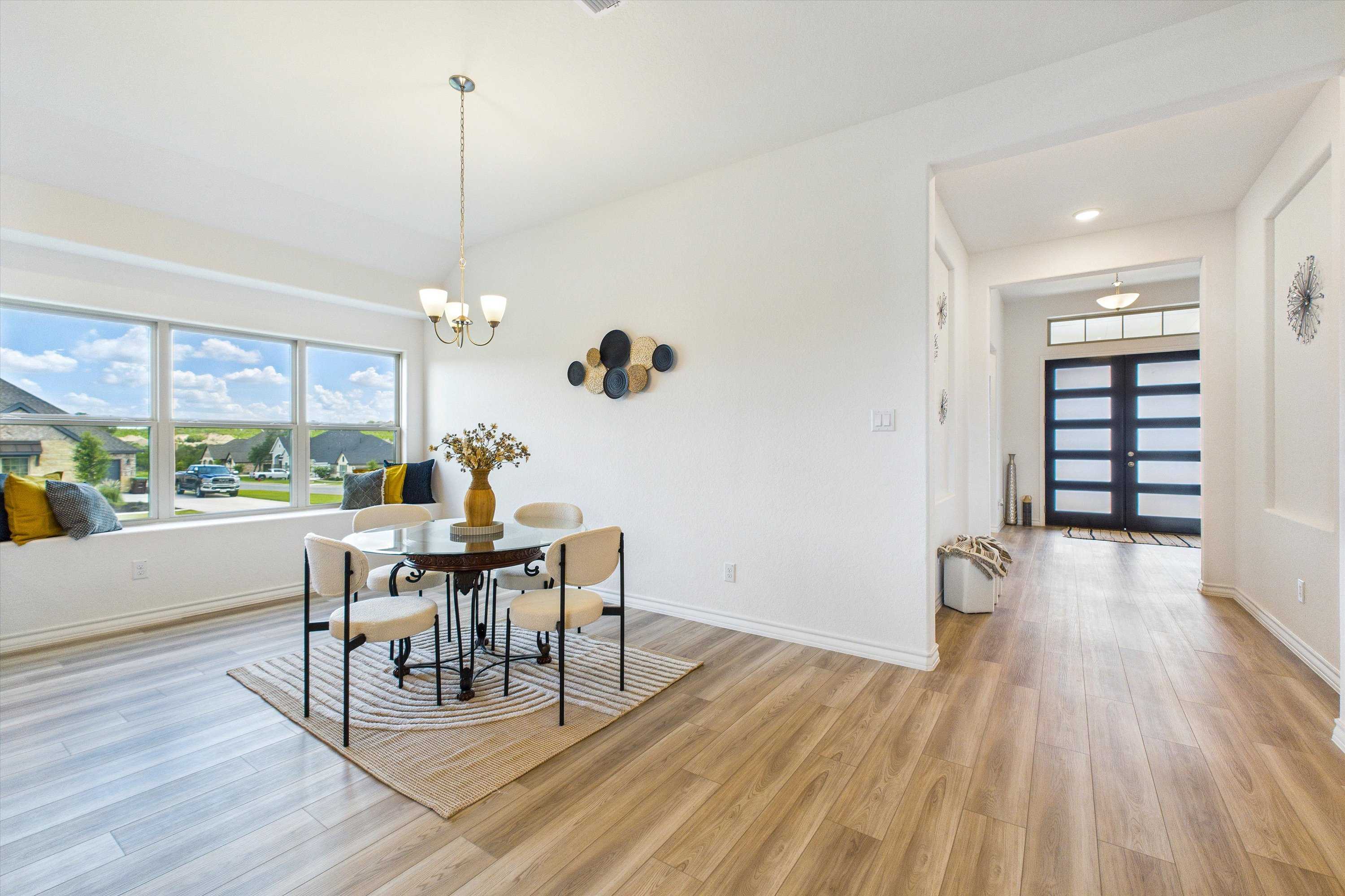 Bright dining nook with round table, wood floors, and large windows overlooking fields in The Summerlin C, Castroville, Texas
