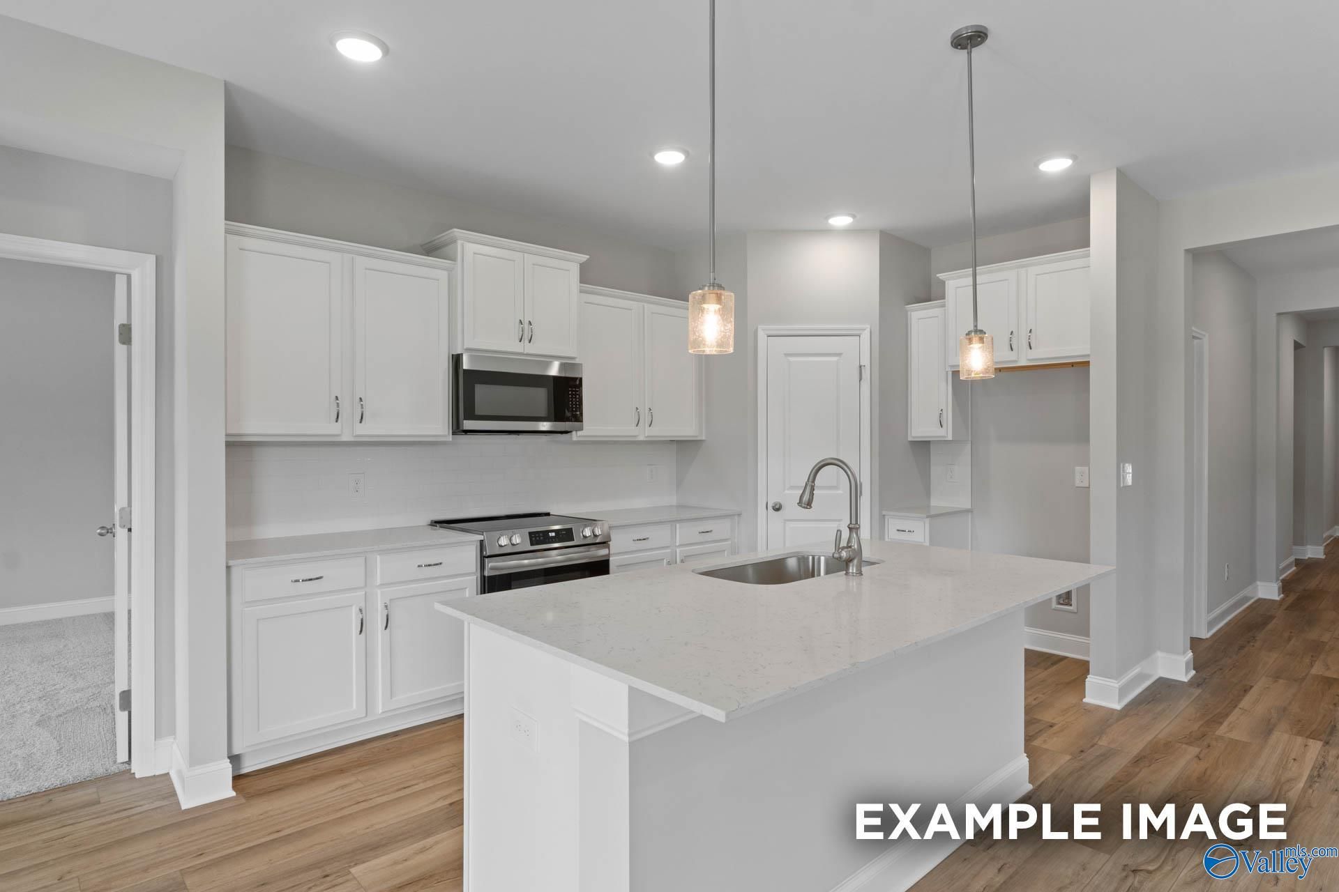 Modern white kitchen with quartz island, stainless steel appliances, and pendant lights in The Everett B floor plan, Athens, AL
