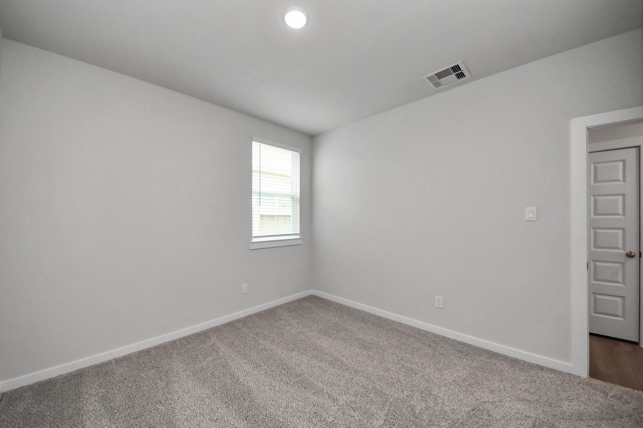 Bright carpeted bedroom with white walls and window in Davidson Homes The Frio F plan at Robins Landing, Houston, Texas