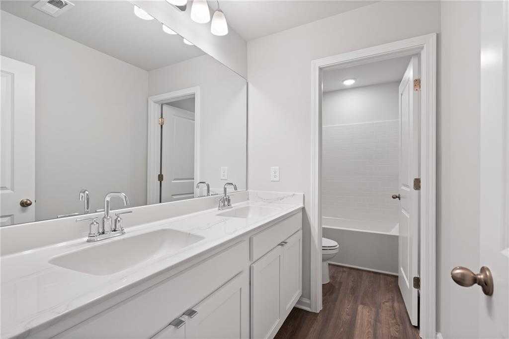 Modern double-sink vanity bathroom with white cabinets, large mirror, and hardwood floors in Davidson Homes The Hickory B, Winder, GA