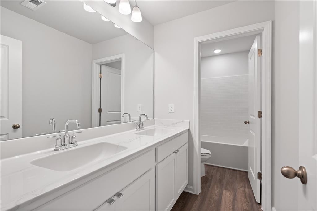 Bright white double vanity bathroom with large mirror, toilet, and hardwood floors in Davidson Homes The Hickory A, Winder, GA