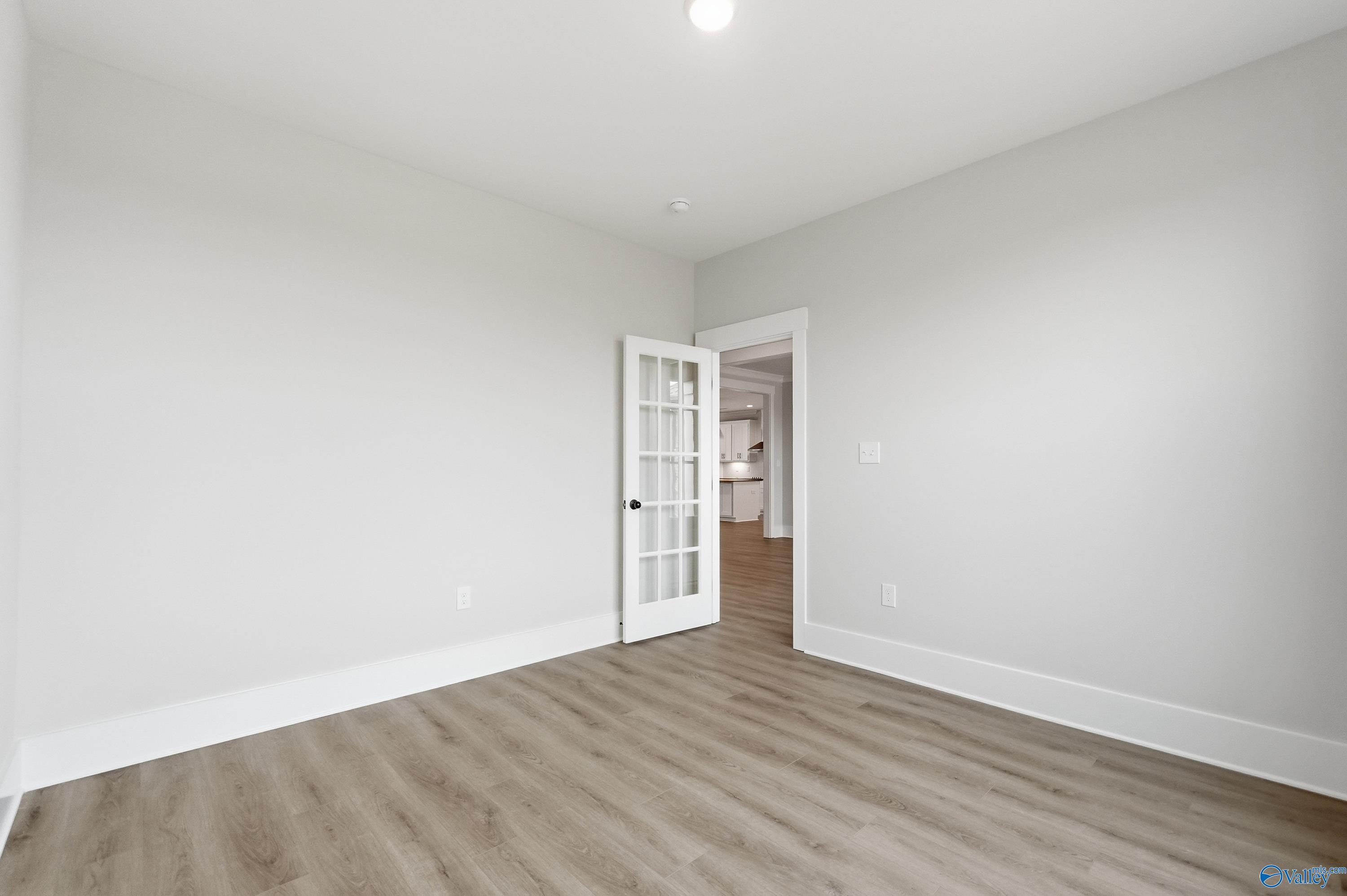 Bright bedroom with light gray walls, hardwood-style floors, and white French doors in Davidson Homes The Finleigh, Meridianville, Alabama