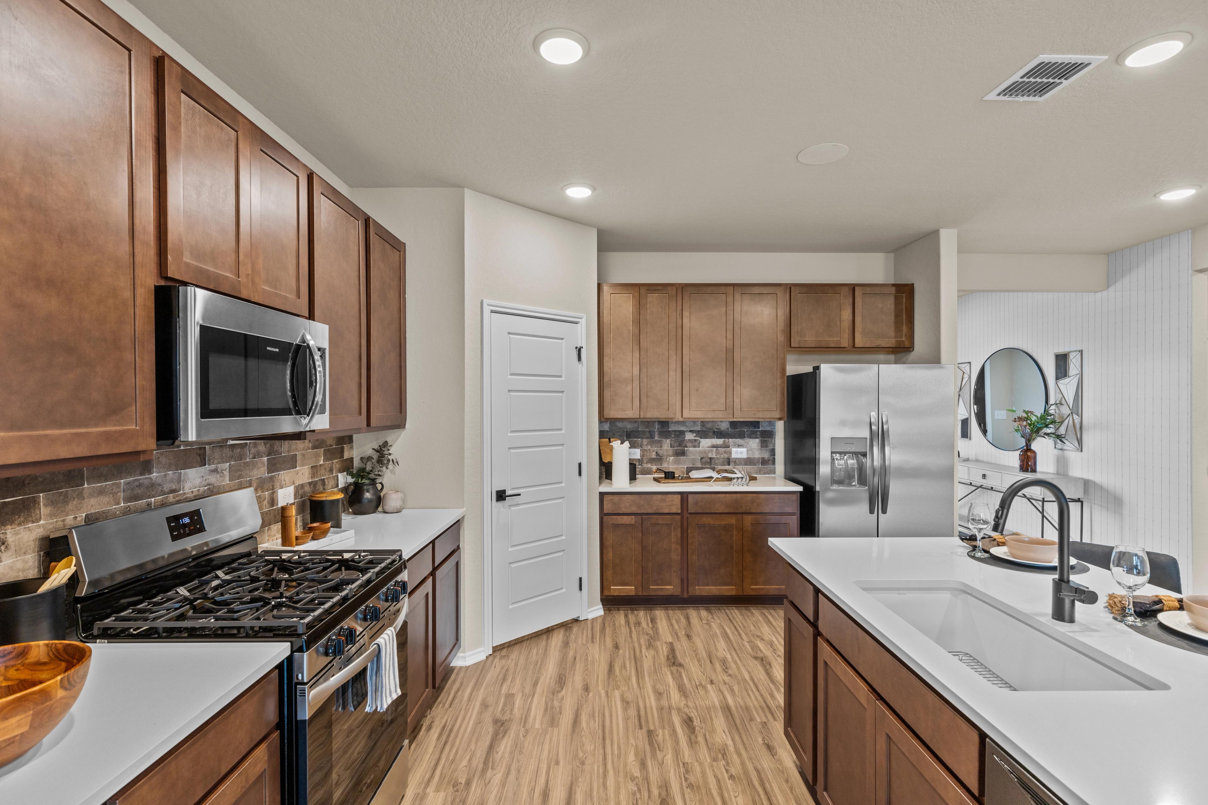 Spacious modern kitchen at Bricewood in San Antonio TX by Davidson Homes with warm wood cabinets, stainless steel appliances, quartz island and hardwood floors