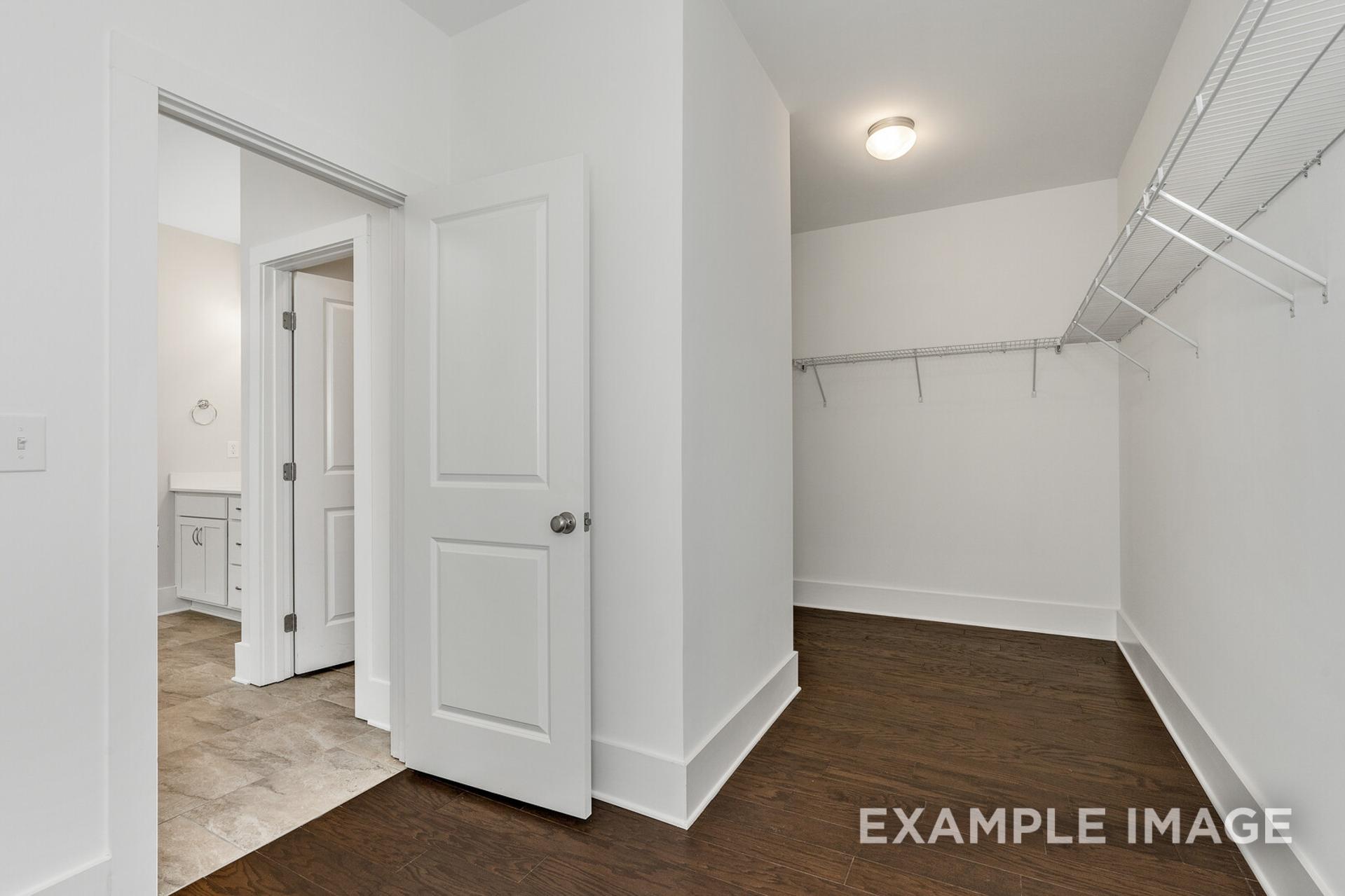 Spacious master walk-in closet in The Rockford home with white shelving, hardwood floors, and adjacent bathroom vanity
