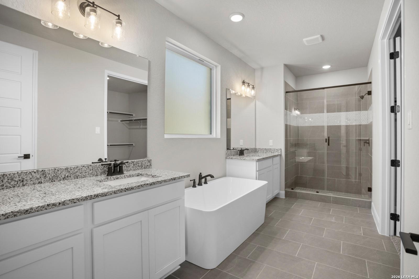 Modern primary bathroom with granite vanity, soaking tub, and glass shower in The Jennings G plan at Ladera, San Antonio.