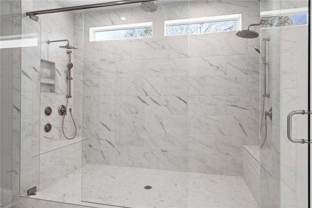 Luxurious master bathroom with frameless glass shower, white marble tiles, rain showerhead, and built-in bench in Davidson Homes Arlington A, East Cobb