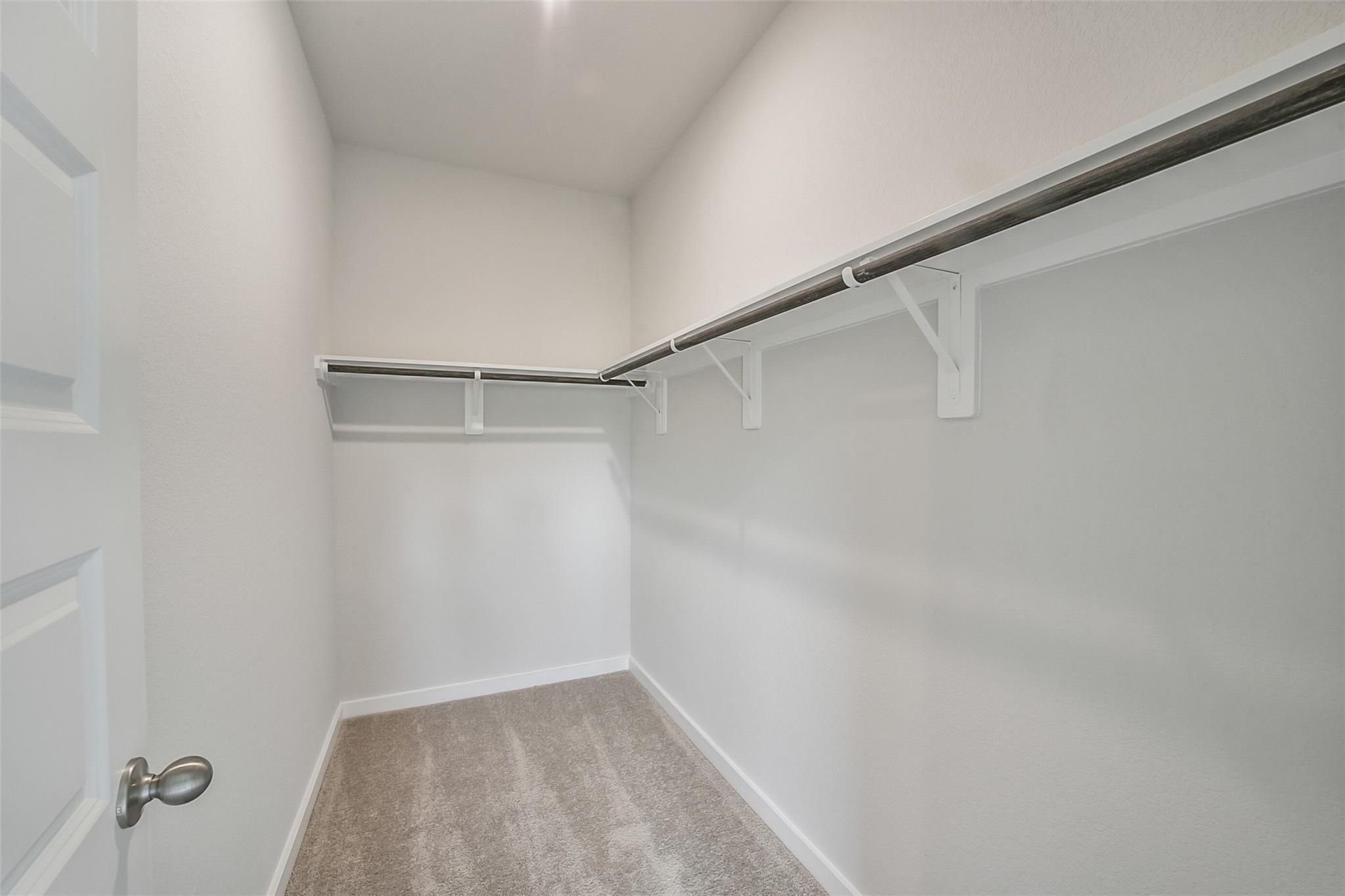 Spacious walk-in closet with white shelving and hanging rods on carpeted floor in Davidson Homes The Frio F, Conroe, TX