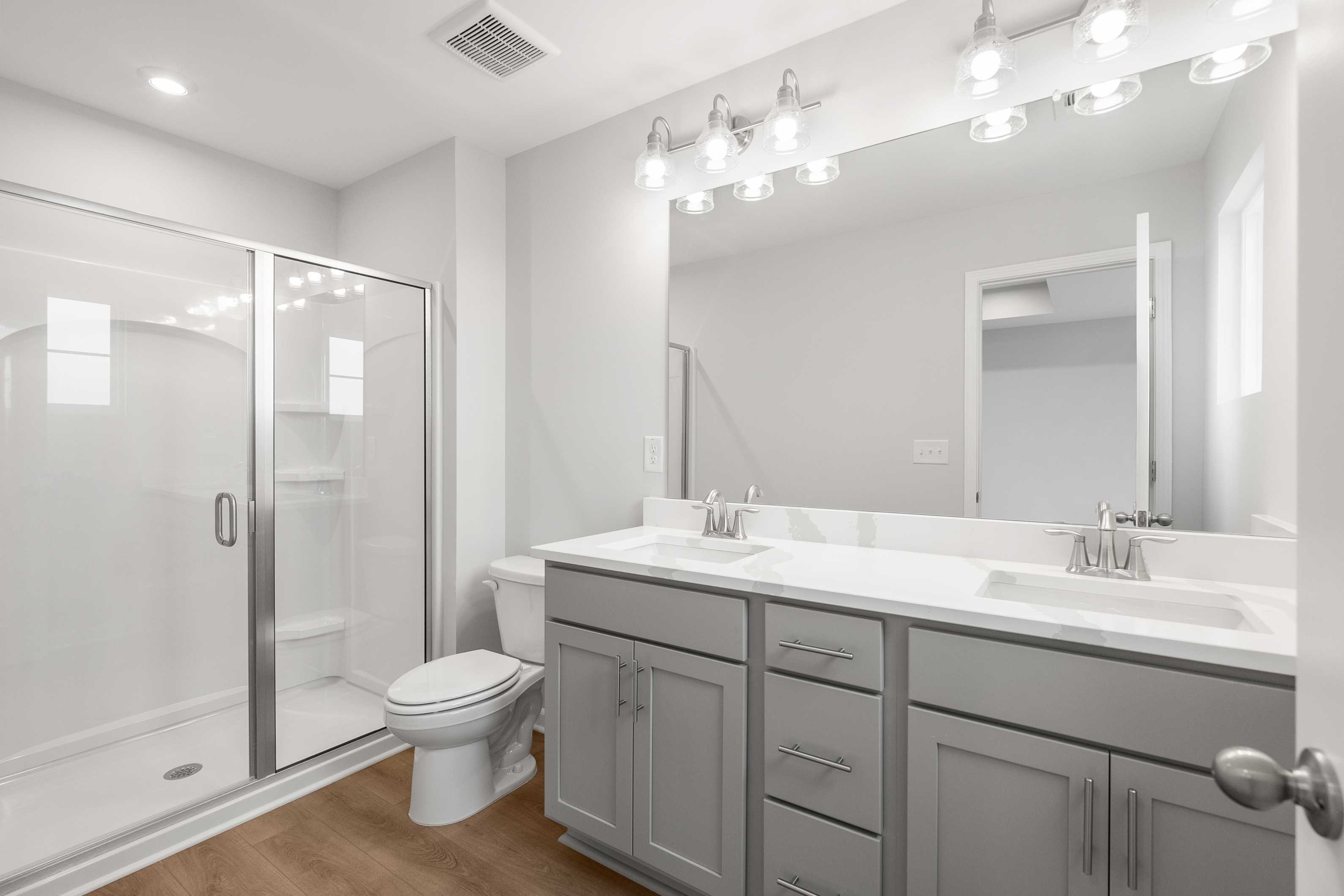 Modern master bathroom in The Durant A with glass shower, double gray vanity, quartz counters, and wood floors