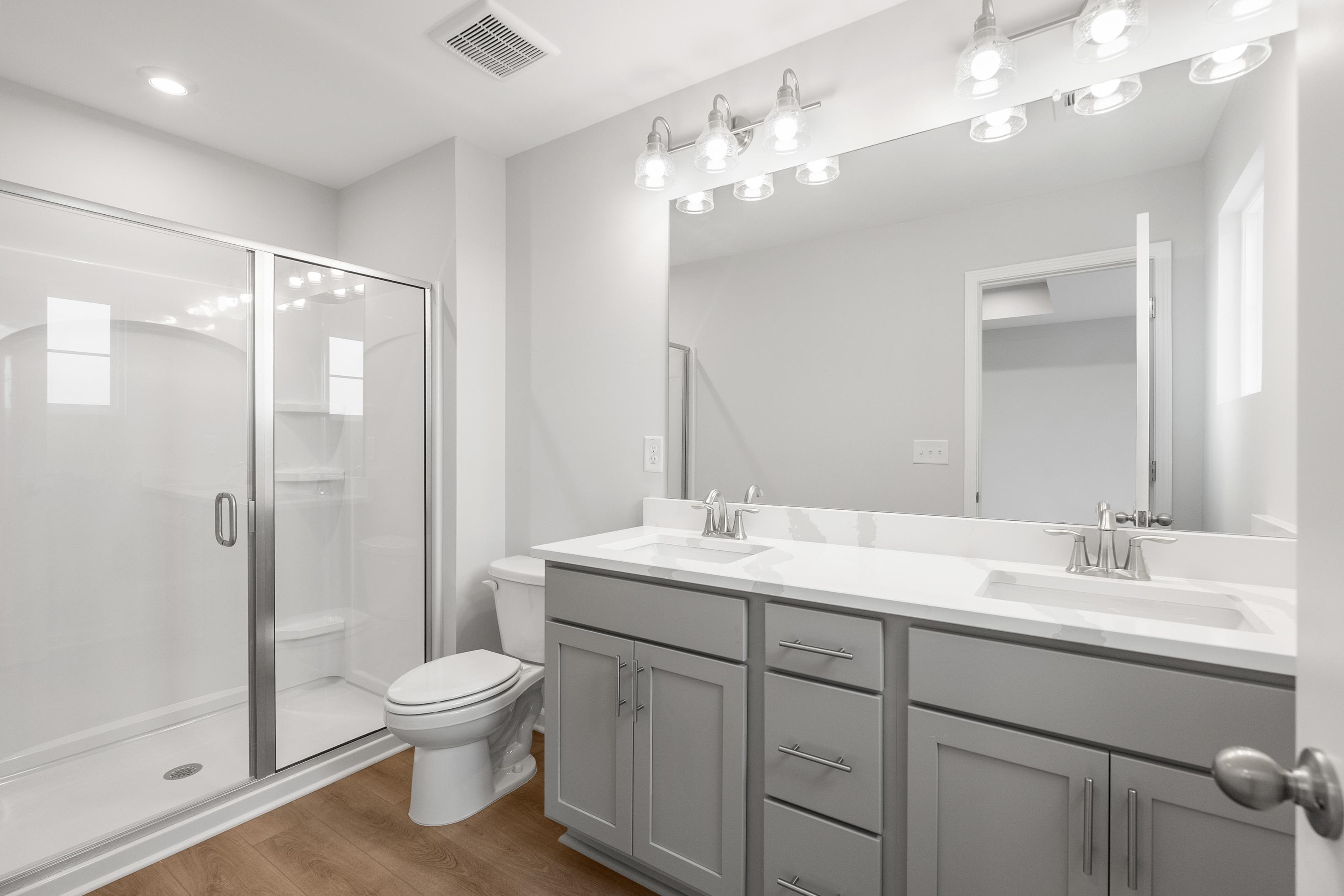 Modern master bathroom in The Durant A with glass shower, double gray vanity, quartz counters, and wood floors