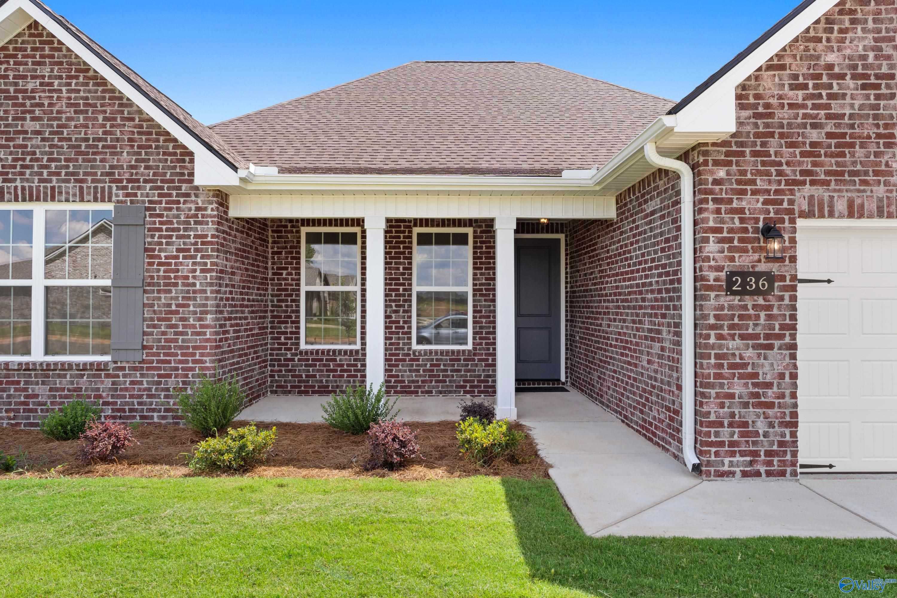 Modern red brick 1-story home with gabled roof, front porch columns, 2-car garage, and landscaped yard in Kendall Downs, Toney, Alabama