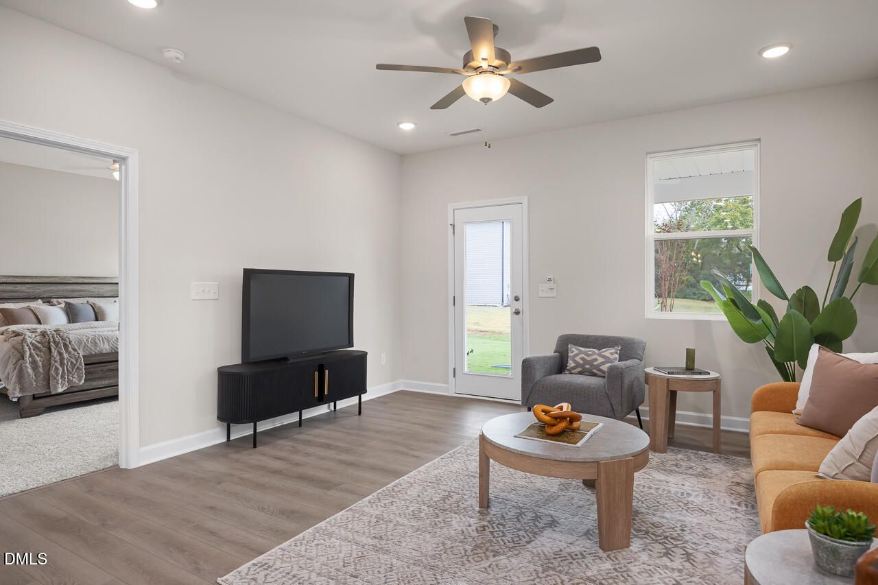 Cozy living room with ceiling fan, flat-screen TV, orange sofa, and sliding doors to backyard in Davidson Homes The Carter C, Lillington, NC