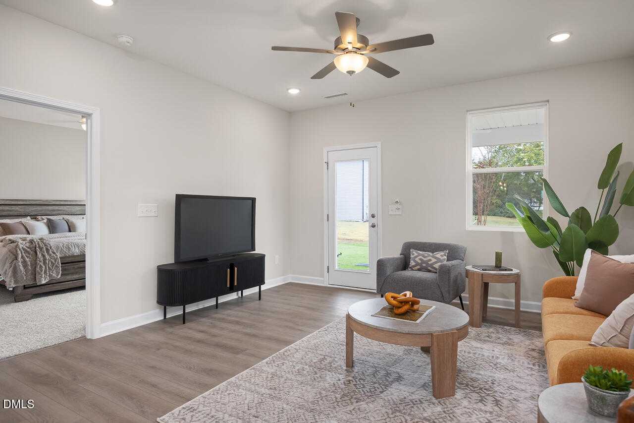Cozy living room with orange sofa, ceiling fan, TV, and sliding door to yard in Davidson Homes The Carter C, Lillington, NC