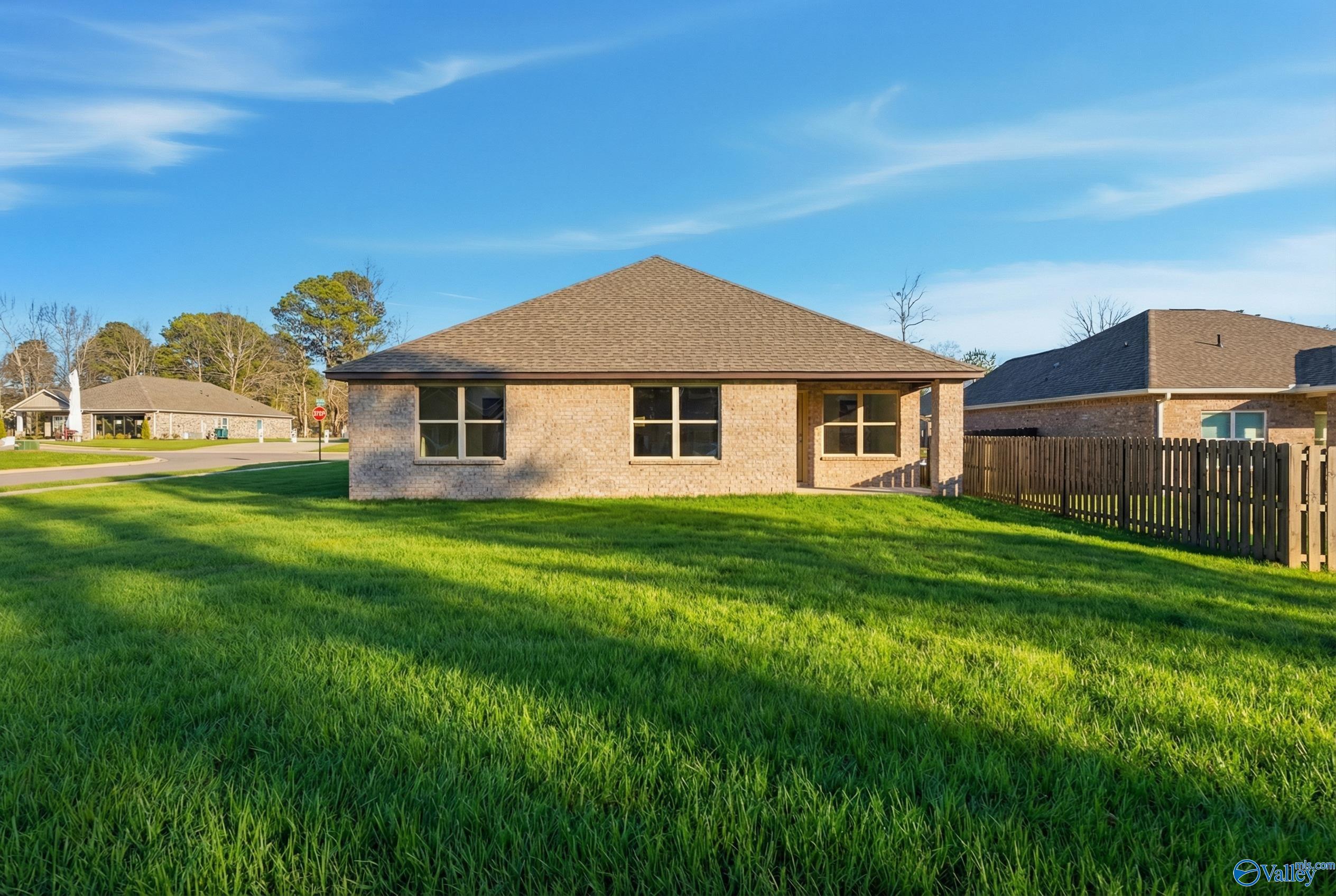 Single-story brick home with gabled roof, large windows, lush green yard, and wooden fence in The Highlands, Arab, Alabama