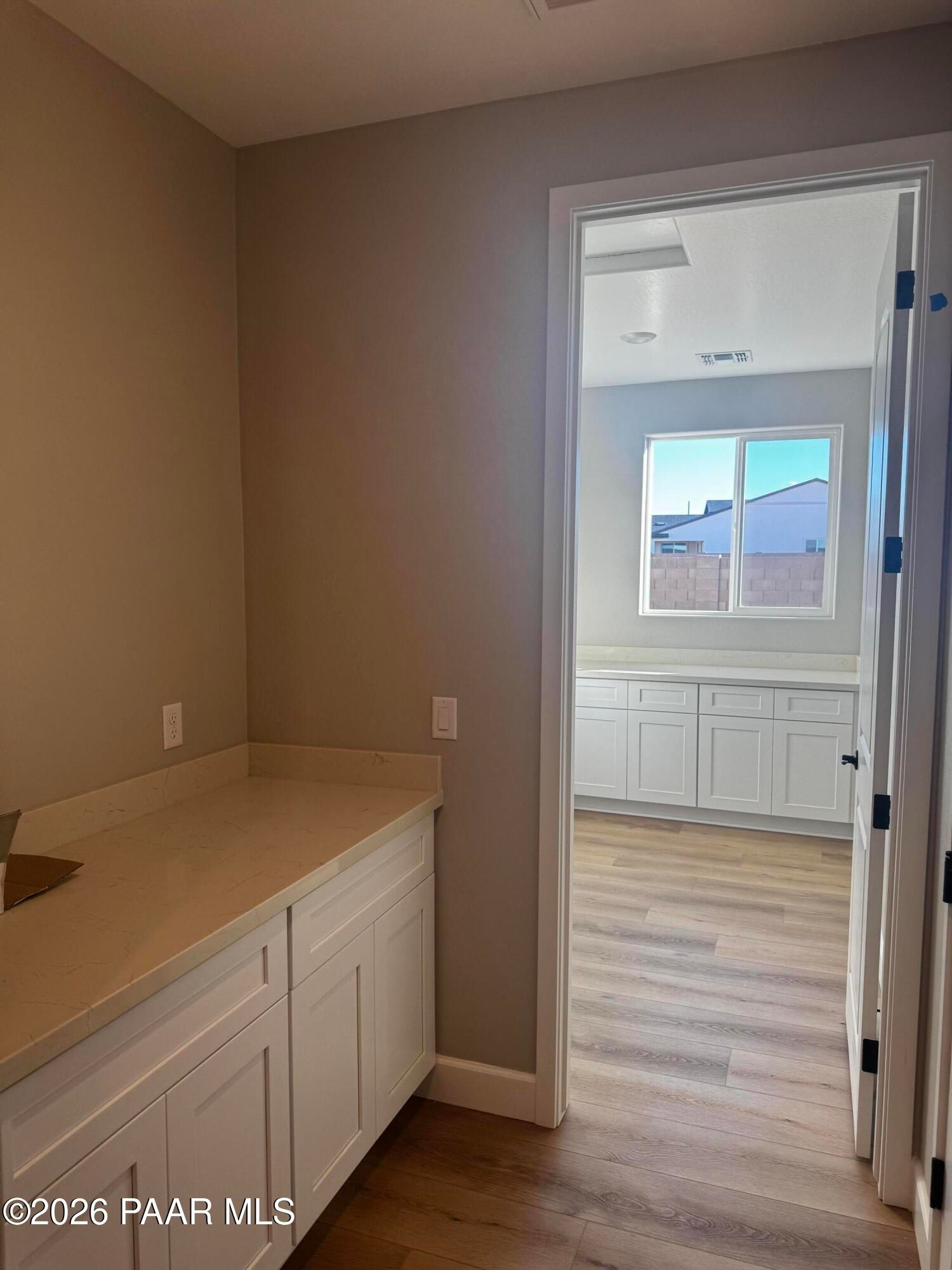 Modern laundry room with white shaker cabinets and quartz countertop adjacent to kitchen in Evermore Homes The Monarch B, Prescott Valley, AZ