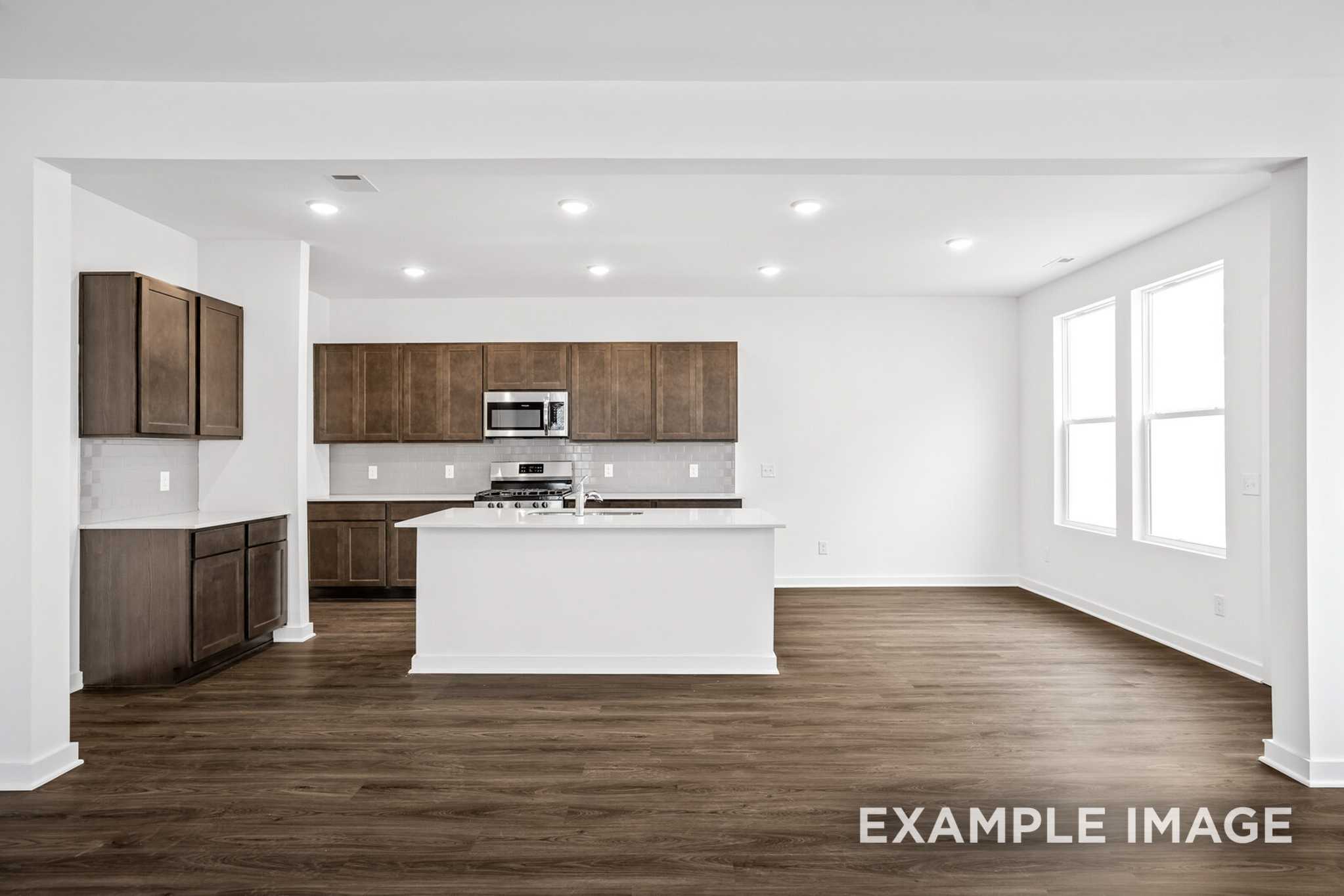 Spacious open-concept kitchen in The Grayson C with white island, shaker cabinets, stainless appliances, and wood floors