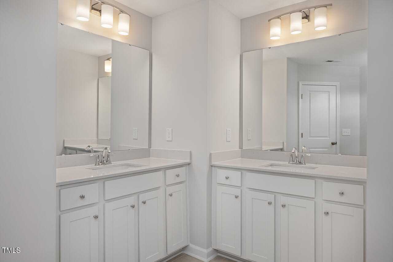 Modern dual-sink vanity with white cabinets, frameless mirrors, and soft lighting in Davidson Homes The Graham, Fuquay-Varina