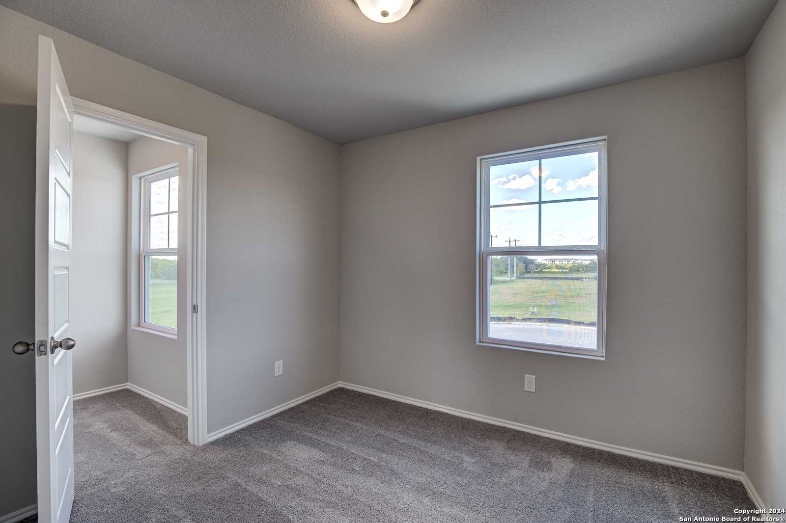 Bright bedroom with neutral gray walls, carpet floor, large window overlooking green fields in Davidson Homes The Blanco C, San Antonio