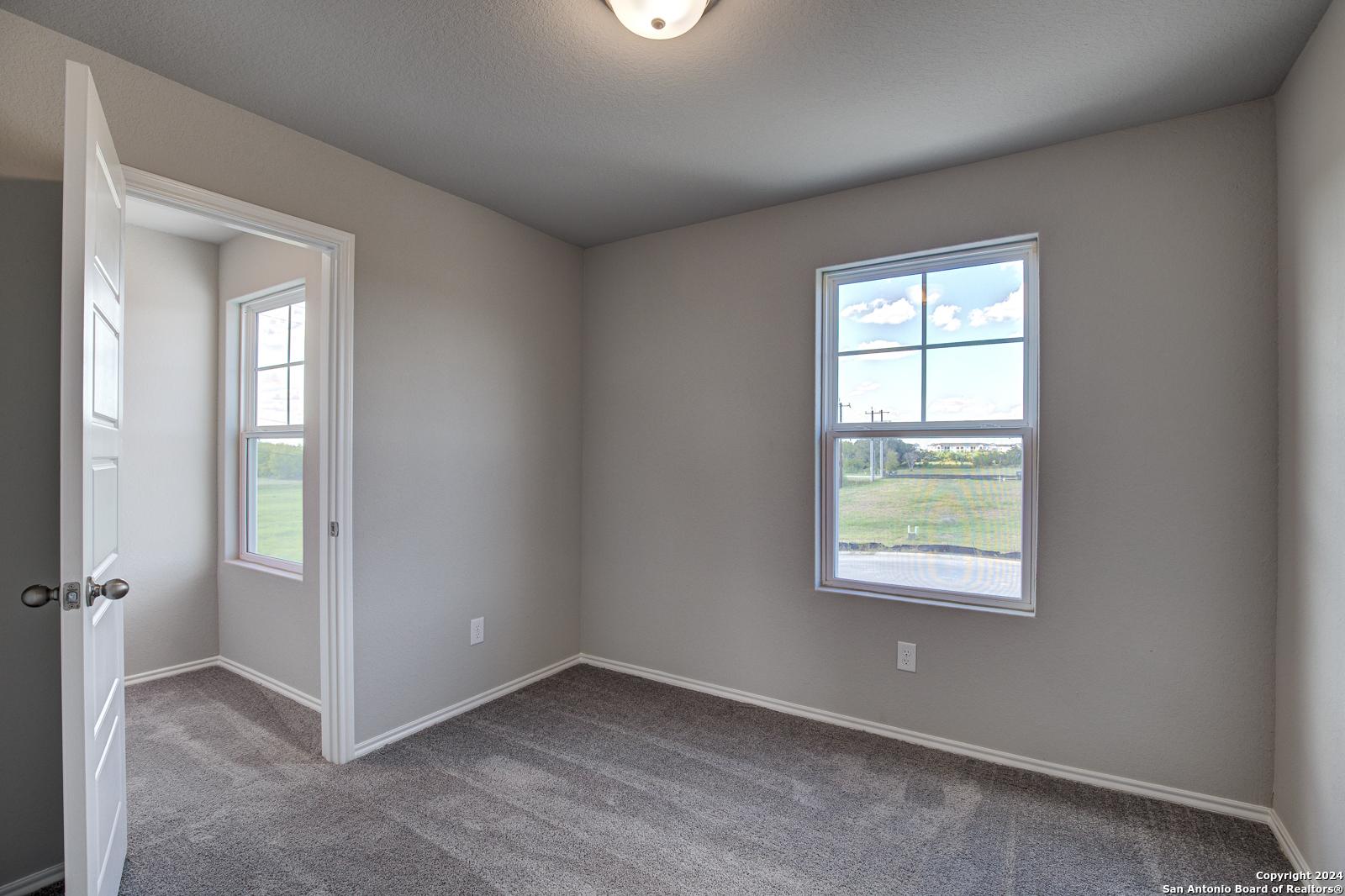 Bright secondary bedroom with beige walls, gray carpet, and large window view of green fields in Davidson Homes The Blanco C, San Antonio