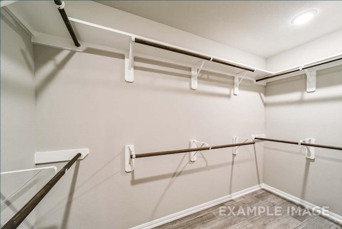 Spacious walk-in closet with white shelving and wooden hanging rods in Davidson Homes The Riviera C, Dayton, Texas