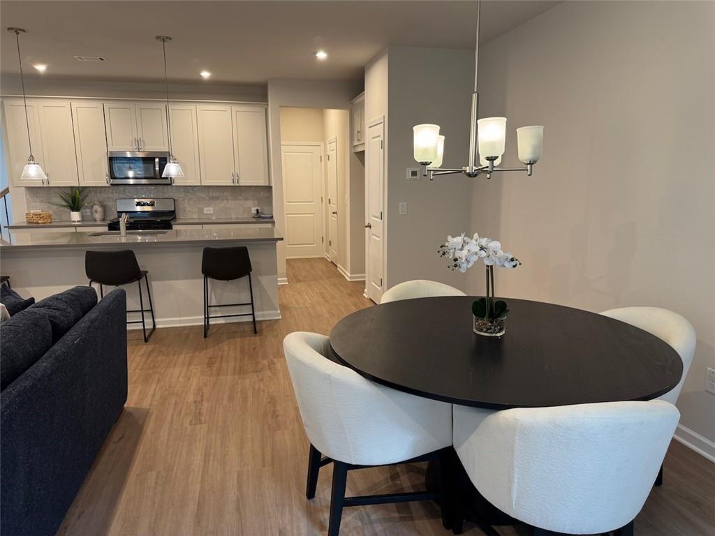 Open-concept dining area with round black table, white chairs, and chandelier next to white kitchen cabinets in The Cary A, Davidson Homes, Kennesaw, GA