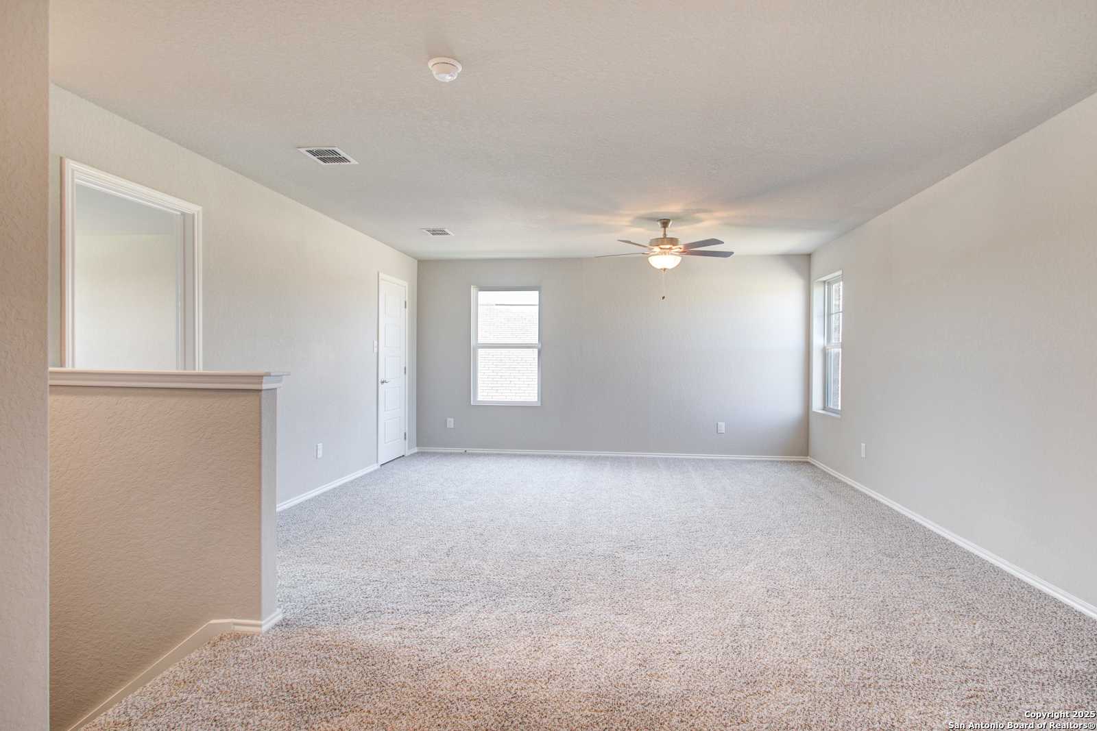 Spacious upstairs loft with beige carpet, ceiling fan, windows, and railing in 4-bedroom Davidson Homes The Douglas G, San Antonio