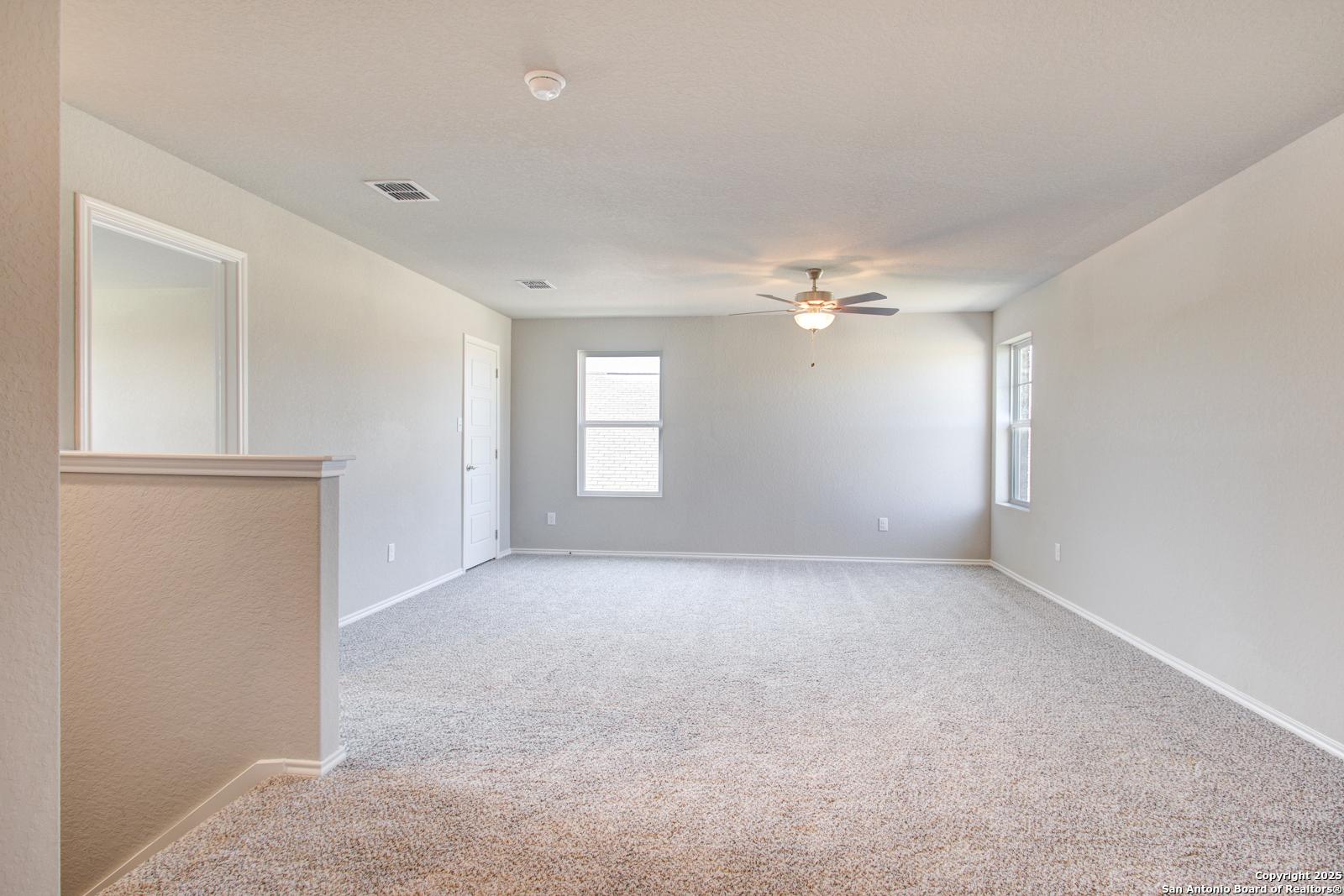 Spacious upstairs loft with beige carpet, ceiling fan, windows, and railing in 4-bedroom Davidson Homes The Douglas G, San Antonio