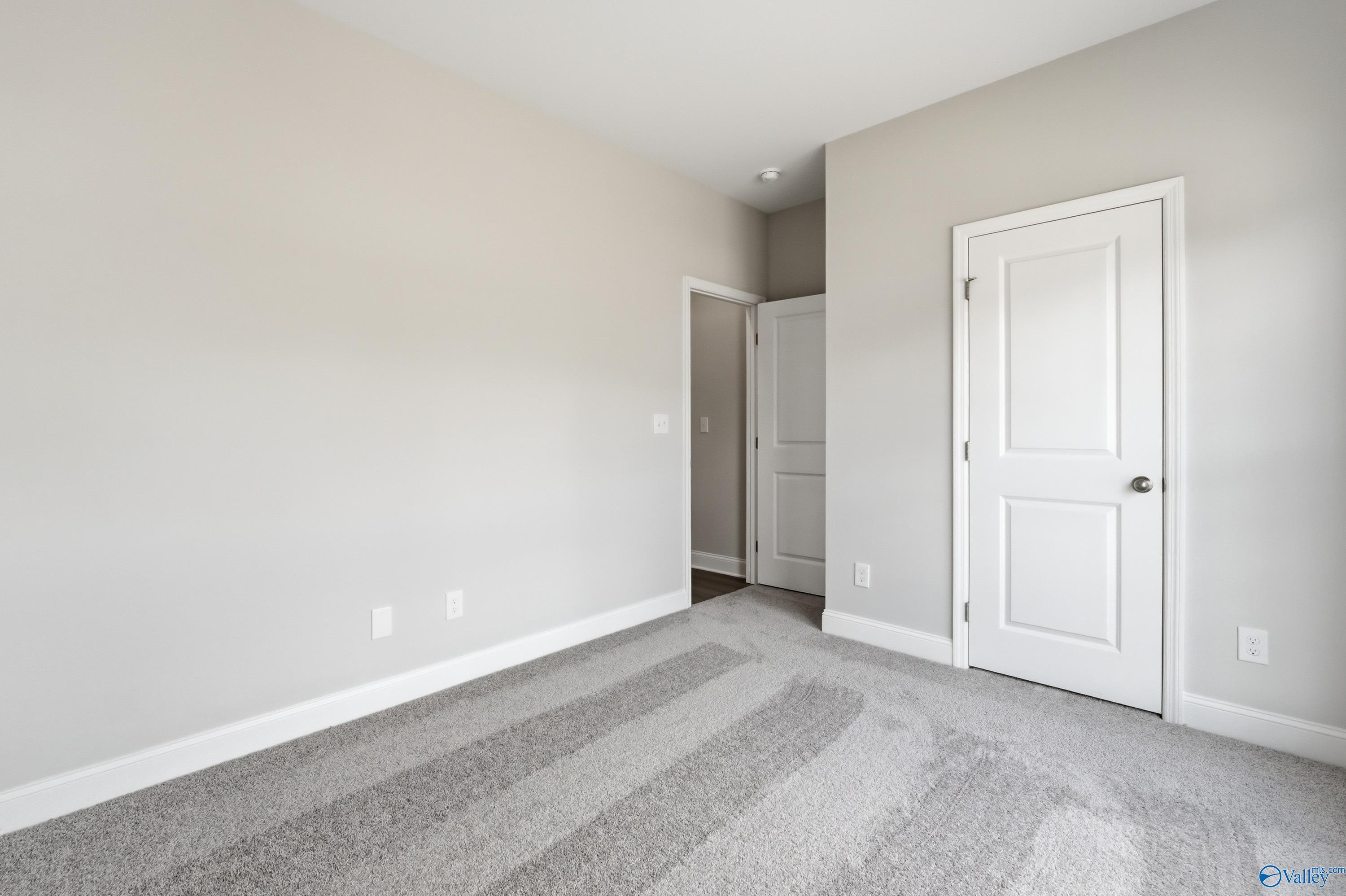 Spacious empty bedroom with neutral beige walls, gray carpet, and white doors in Davidson Homes The Asheville C, Huntsville AL