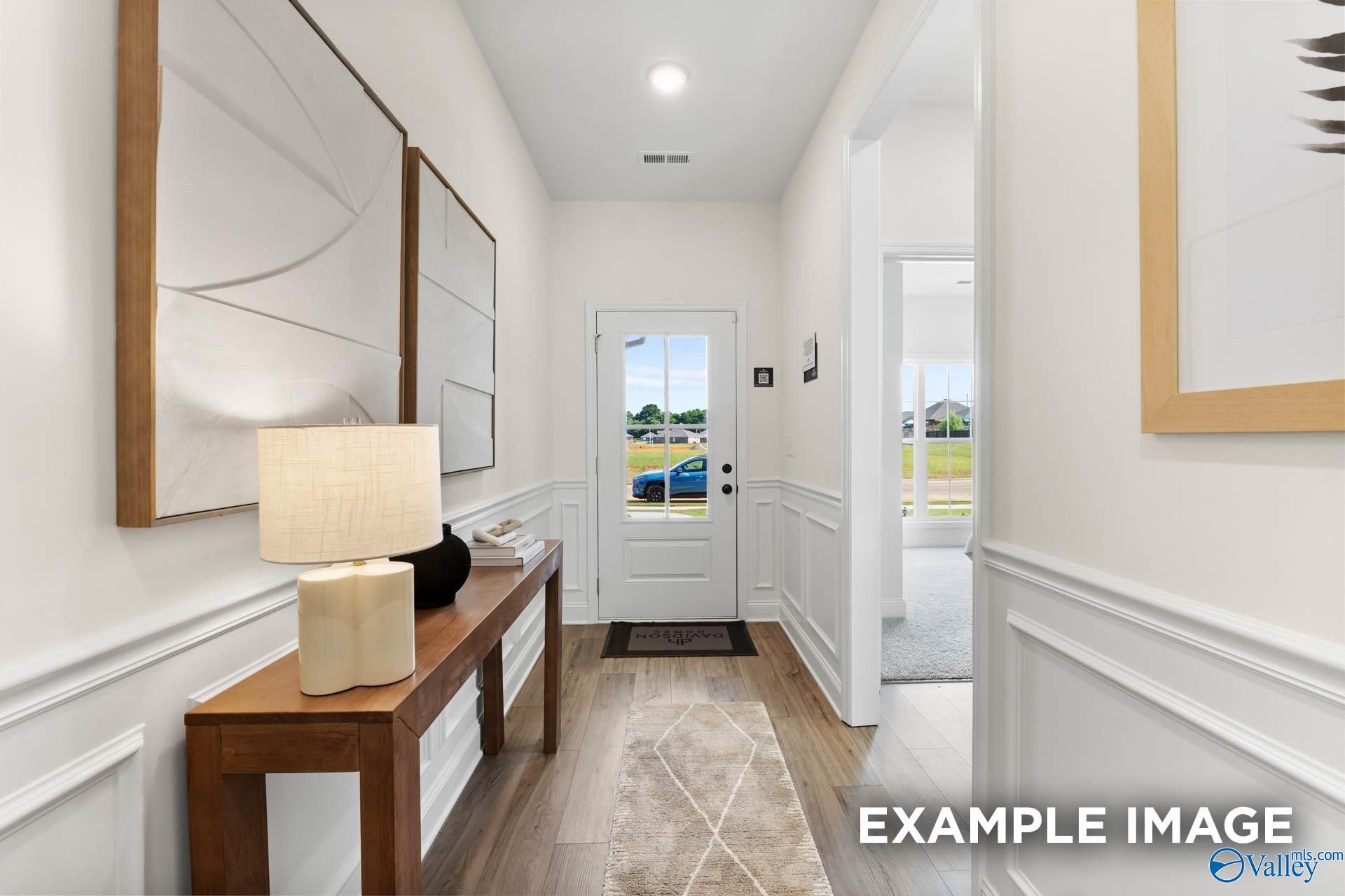 Bright entry hallway with wainscoting, wooden console table, lamp, and glass-front door in Davidson Homes The Franklin, Jaguar Hills, Huntsville