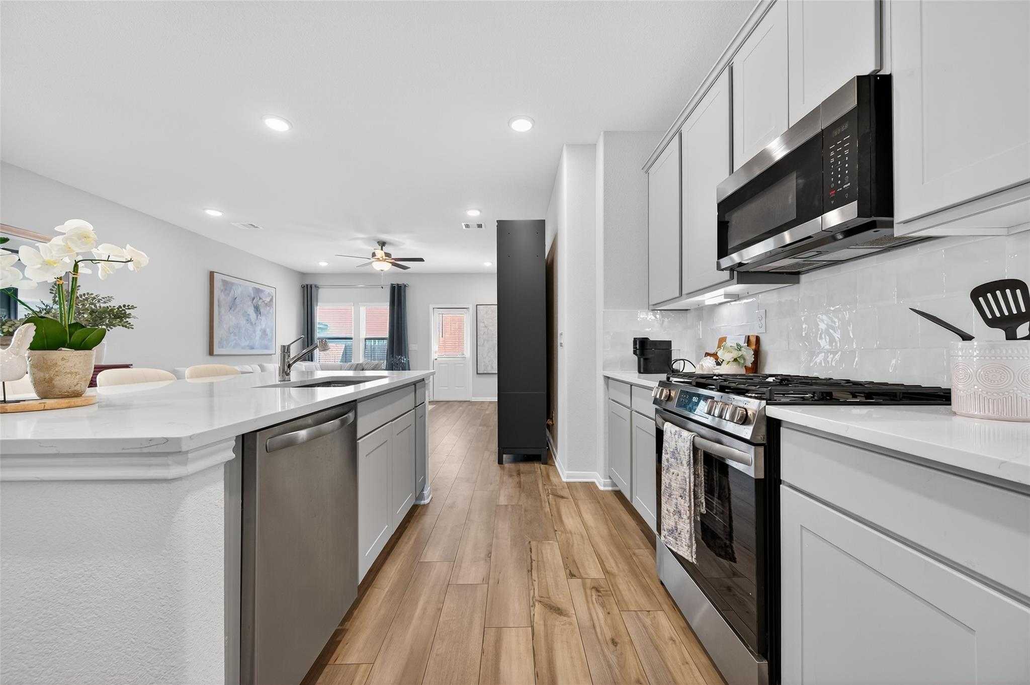 Modern open-concept kitchen with white shaker cabinets, quartz island, stainless appliances in Davidson Homes The Brazos E, Magnolia TX