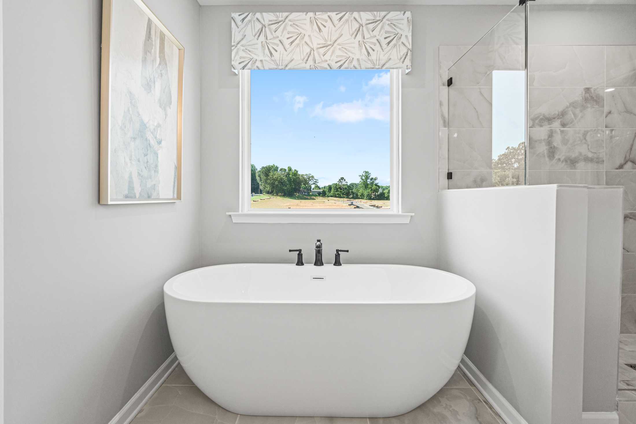 Luxury master bathroom in The Hickory A featuring freestanding white tub, scenic window view, and frameless glass shower