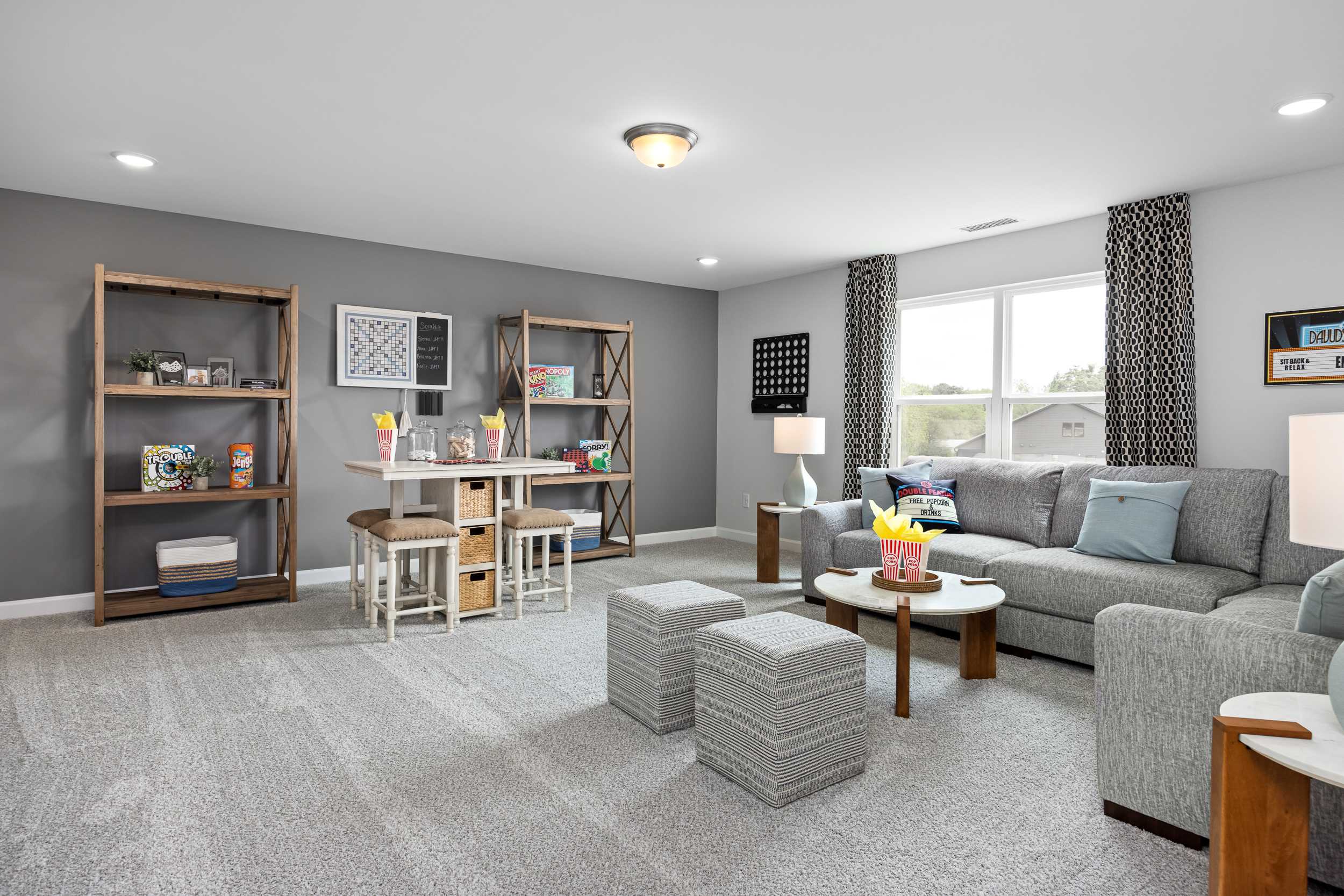 Cozy playroom at Tobacco Road in Angier NC by Davidson Homes featuring bookshelves, kids table, gray sofa, and large windows