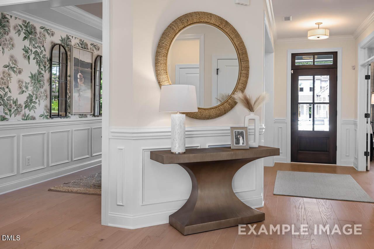 Elegant foyer with gold-framed round mirror, wooden console table, lamps, floral wallpaper in Davidson Homes Crawford D, Angier, NC