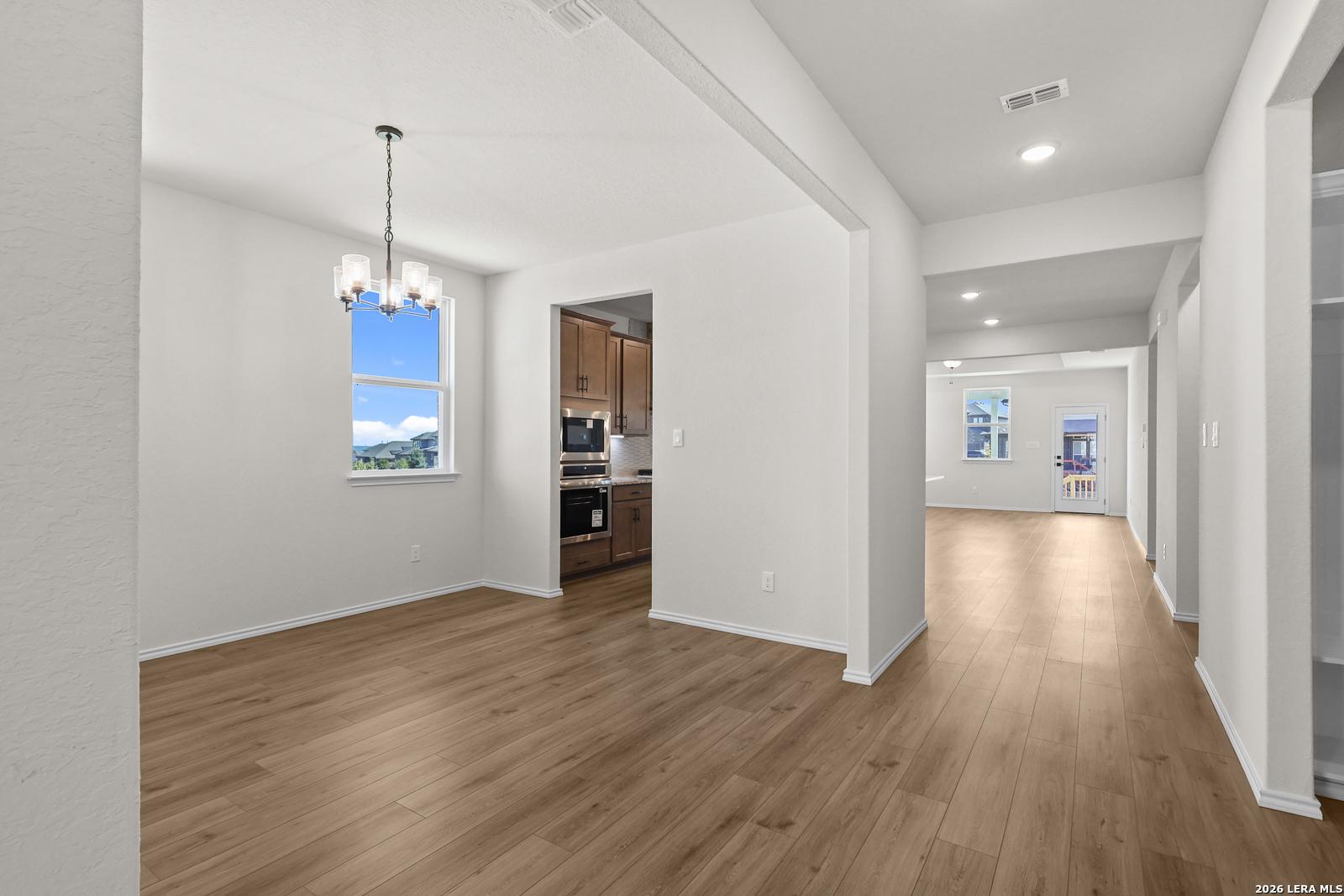 Bright dining area with chandelier and wood-look flooring flowing into kitchen and living room in Davidson Homes Glenwood E, San Antonio