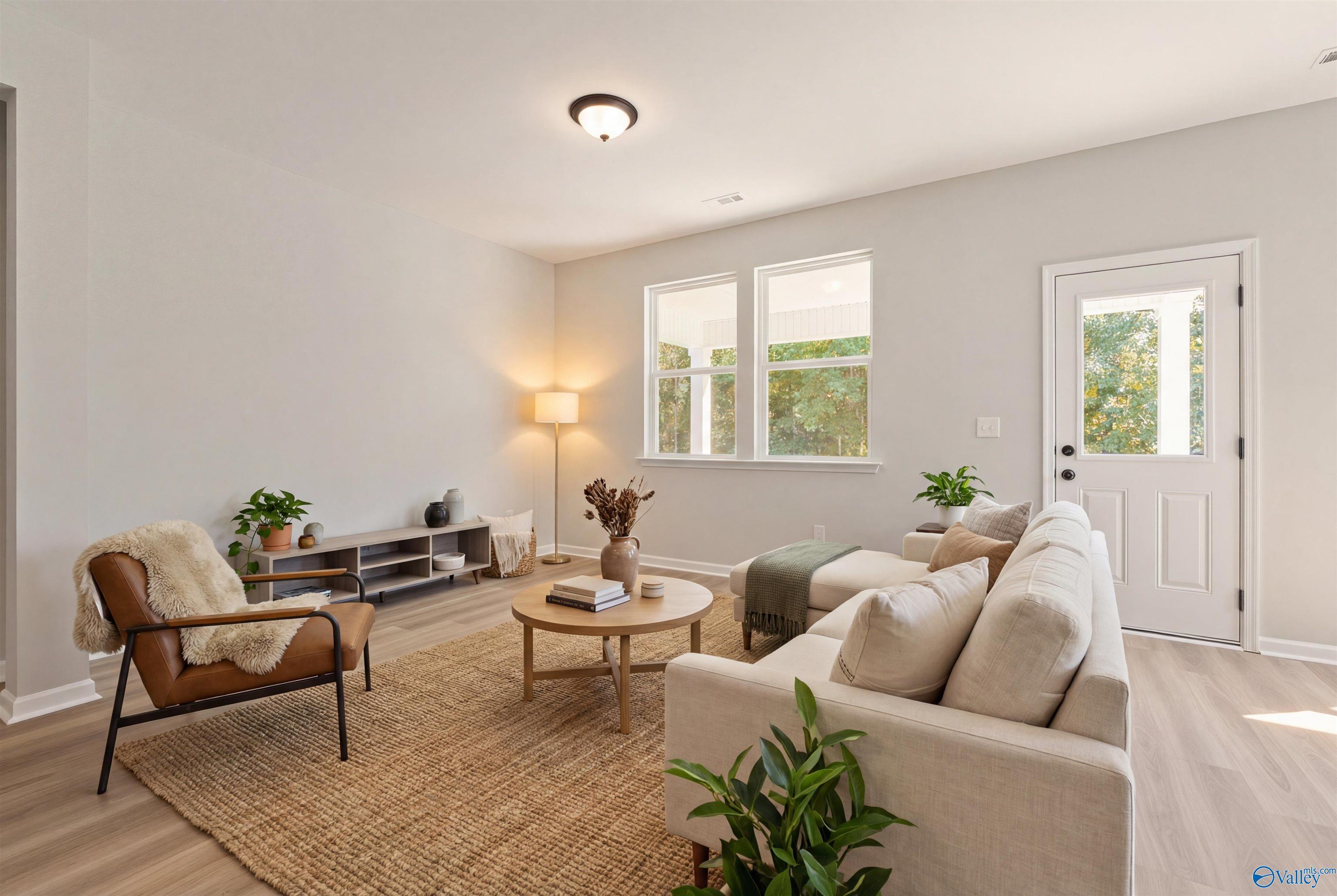 Cozy living room with beige sofa, round wooden coffee table, armchair, plants, and large windows in Davidson Homes The Phoenix, Fayetteville TN