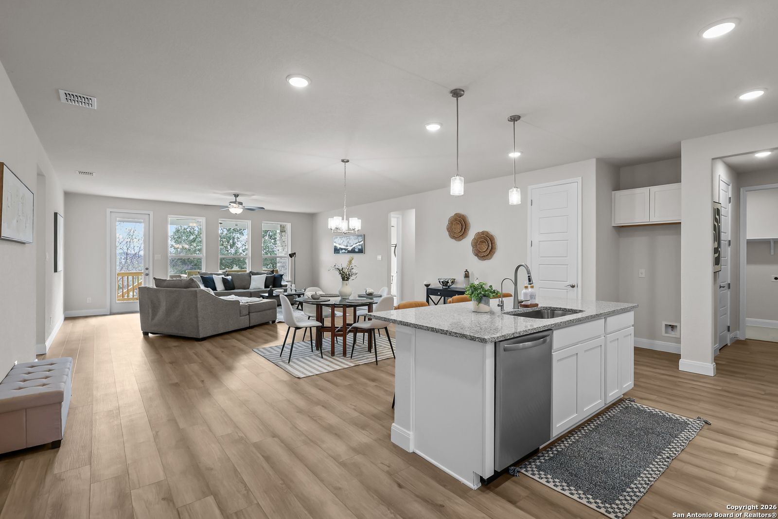Open-concept living and kitchen area with white island, dining table, and sofa in The Lanier H by Davidson Homes, Ladera, San Antonio