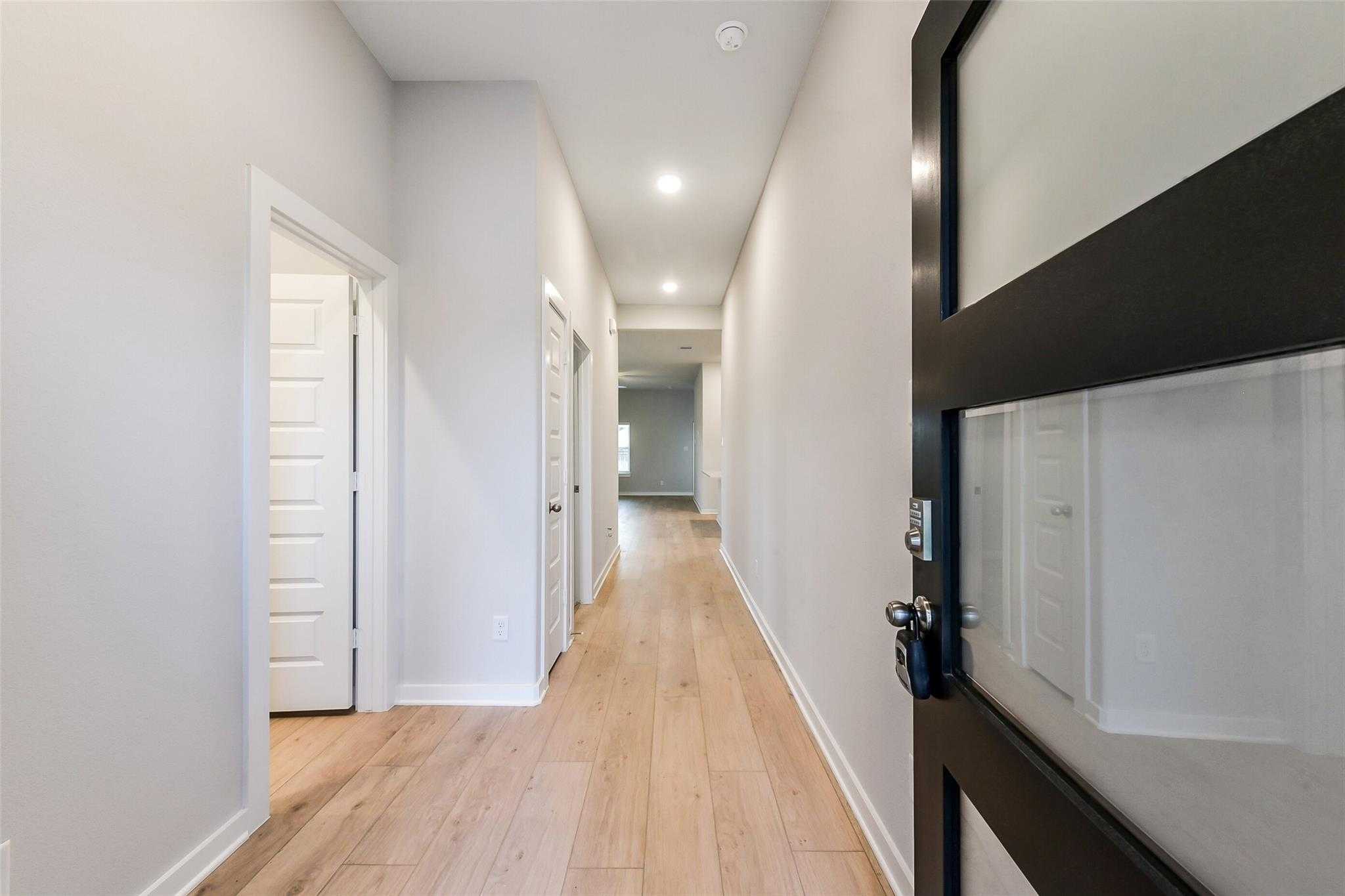 Spacious hallway with oak hardwood floors, light gray walls, and white doors in Davidson Homes The Laguna B, Sunterra, Katy, Texas