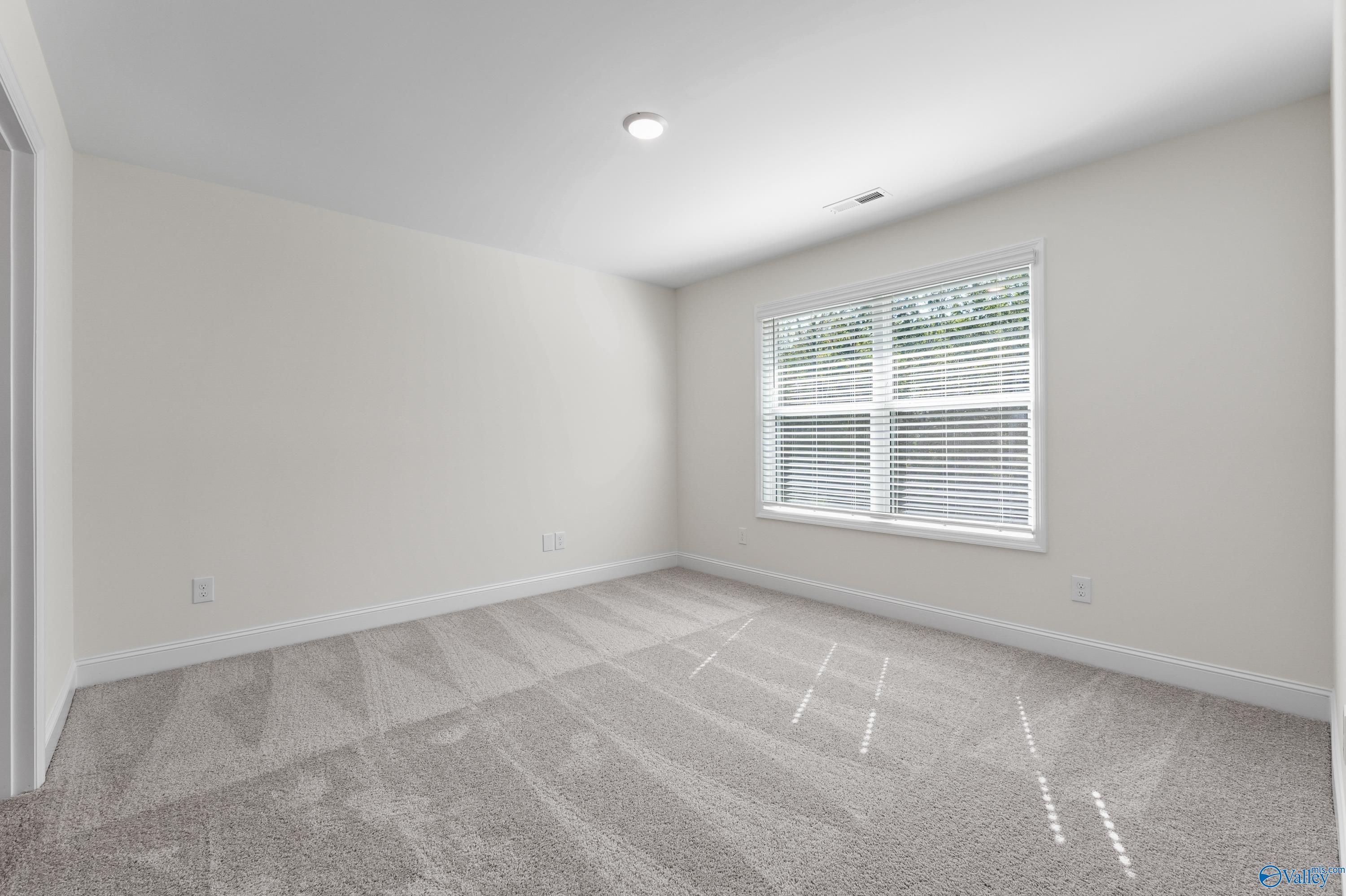 Bright secondary bedroom with neutral walls, plush gray carpet, and large window with blinds in Davidson Homes The Shelby A, Athens, Alabama