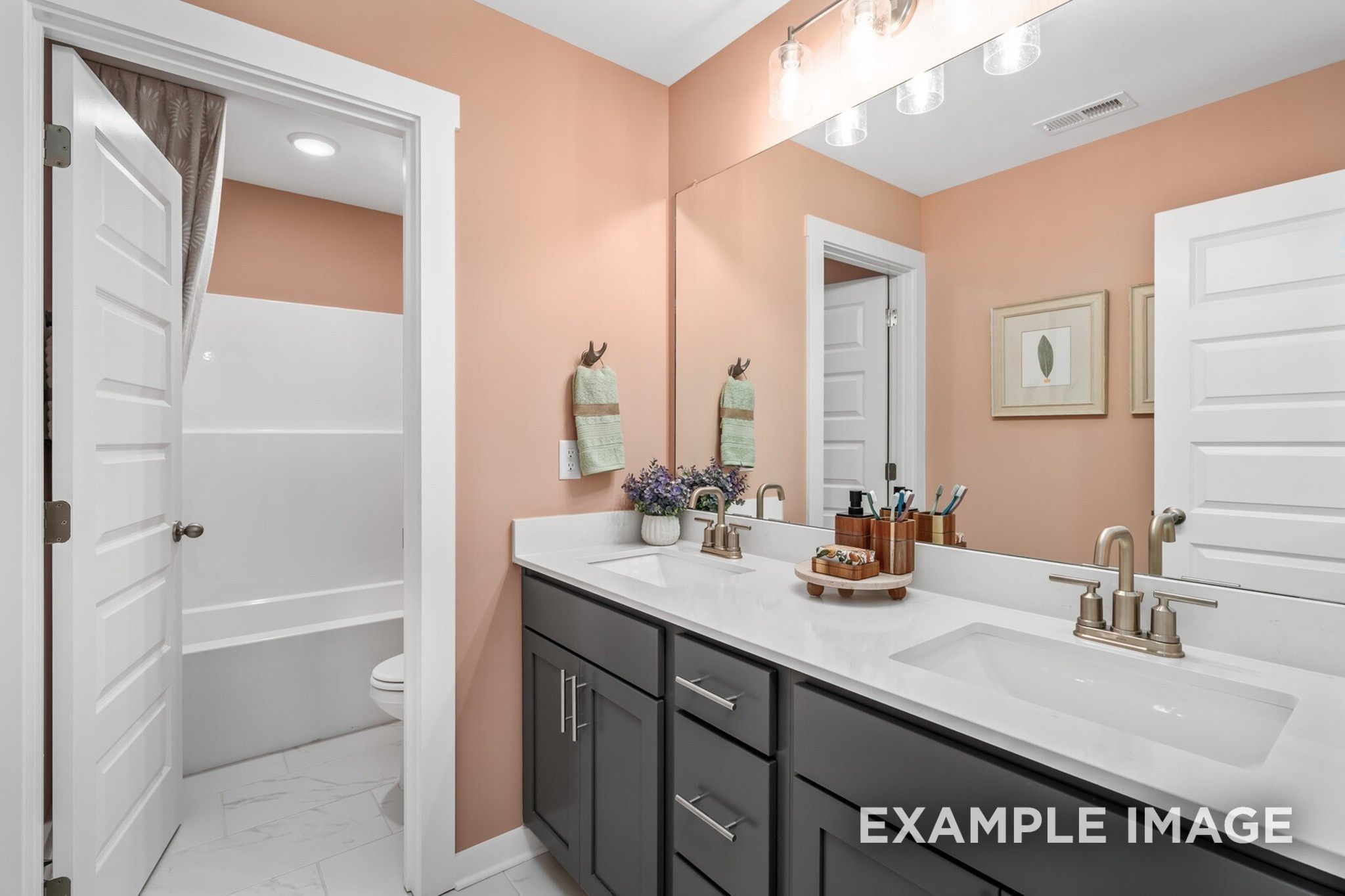 Modern bathroom with dual vanity, quartz countertops, and tub-shower combo in The Ash A home at Woods Crossing, Gallatin.