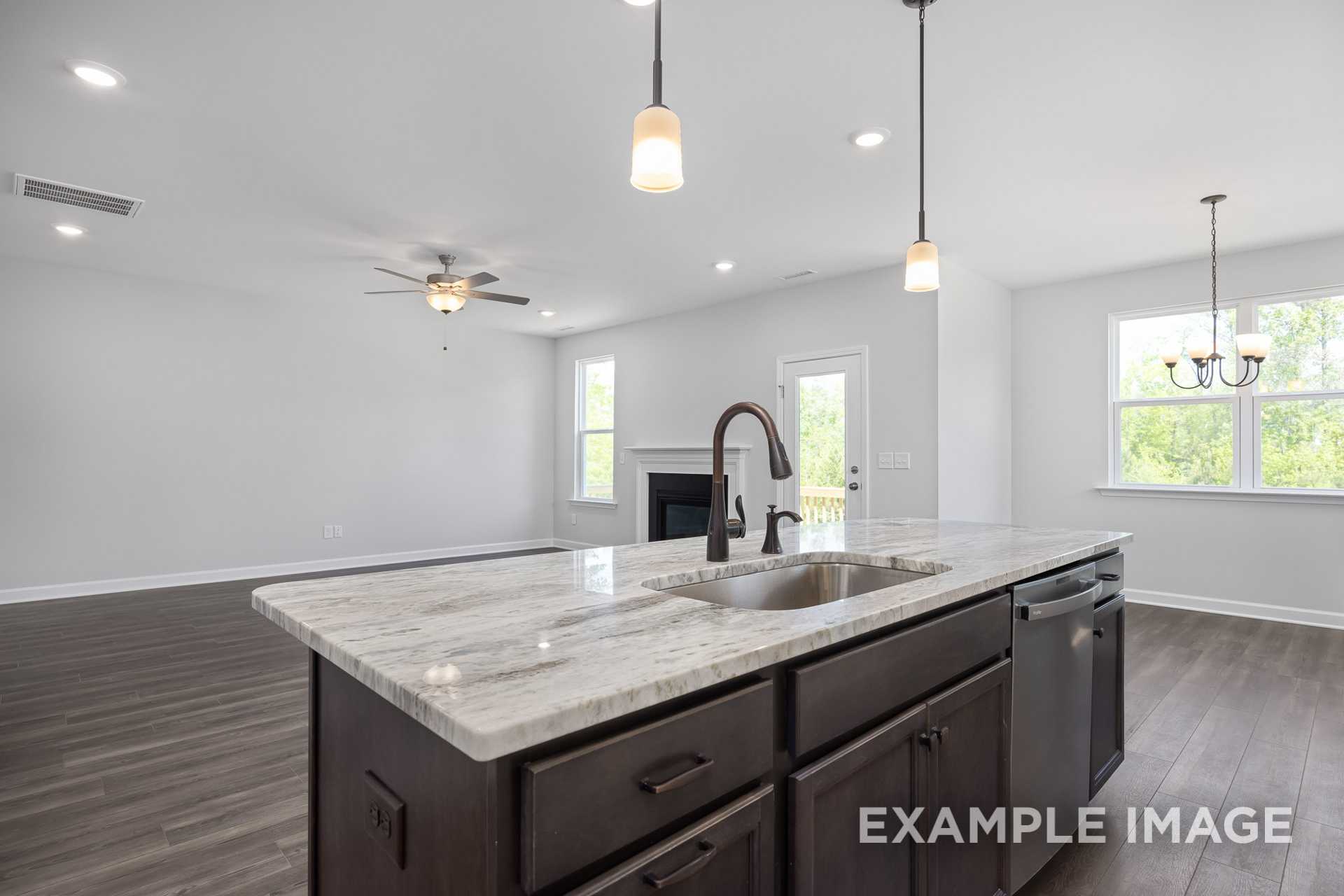 Open-concept kitchen in The Grace C home with quartz island, dark cabinets, pendant lights, and adjacent living area featuring fireplace
