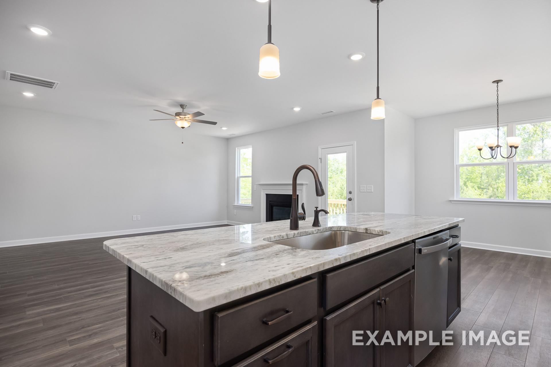 Open-concept kitchen in The Grace C home with quartz island, dark cabinets, pendant lights, and adjacent living area featuring fireplace