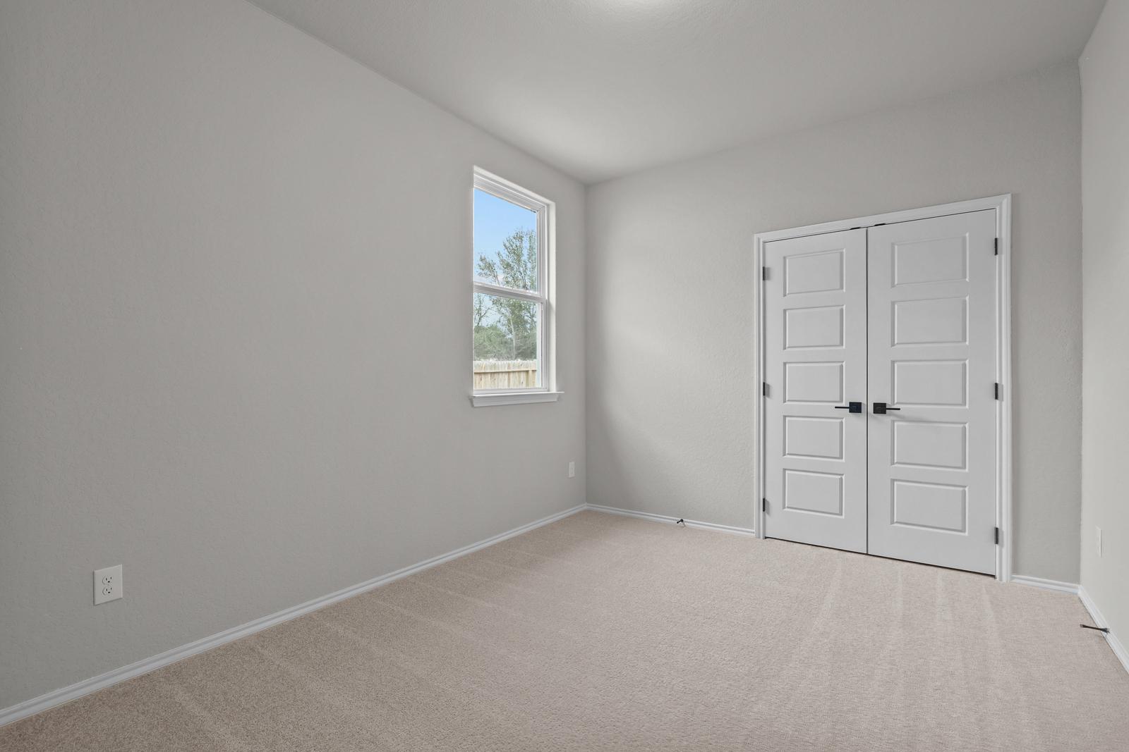 Bright bedroom in The Glenwood E by Davidson Homes featuring neutral carpet, soft wall tones, and double closet doors.