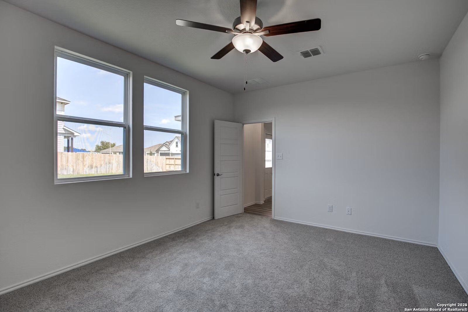 Bright secondary bedroom with ceiling fan, large windows overlooking backyard, and gray carpet in Davidson Homes The Douglas B, Seguin, Texas