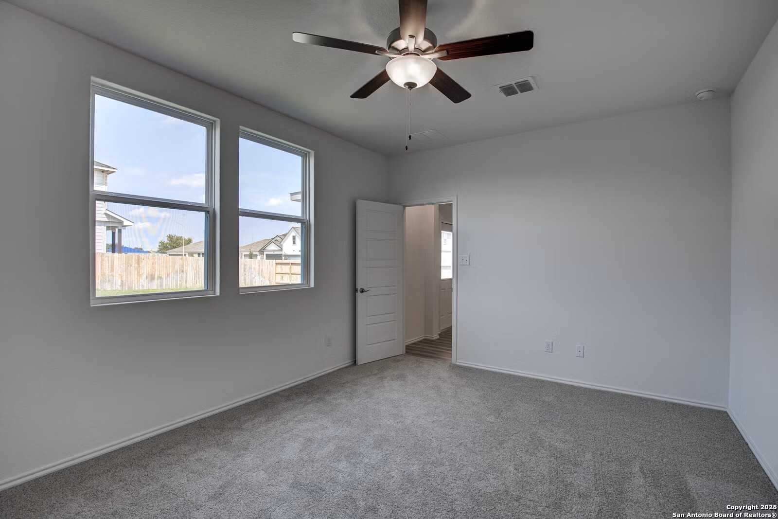 Bright secondary bedroom with ceiling fan, large windows overlooking backyard, and gray carpet in Davidson Homes The Douglas B, Seguin, Texas