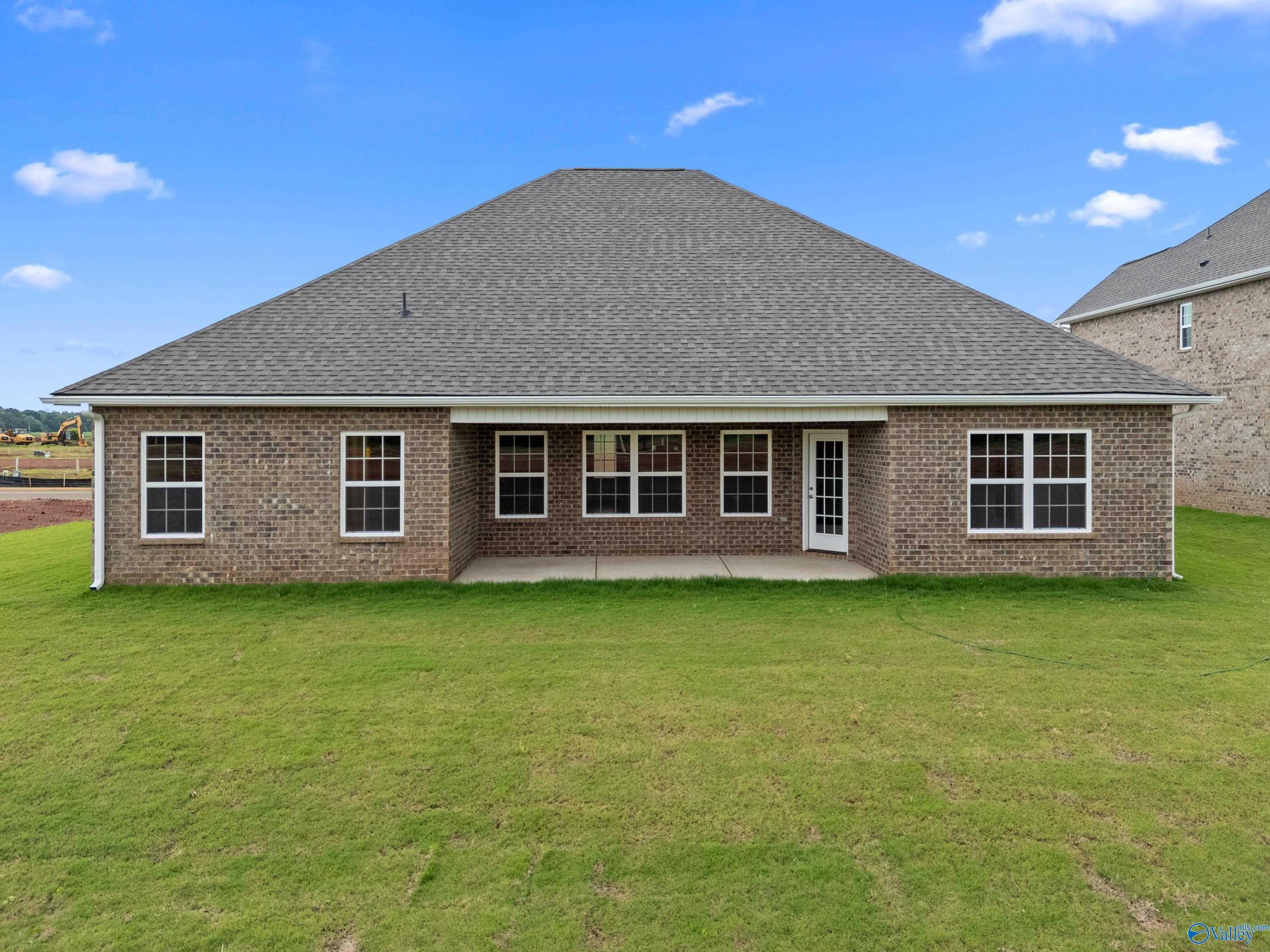 Rear view of brick single-story home with covered patio, large windows, and green lawn in Kendall Farms, Toney, Alabama