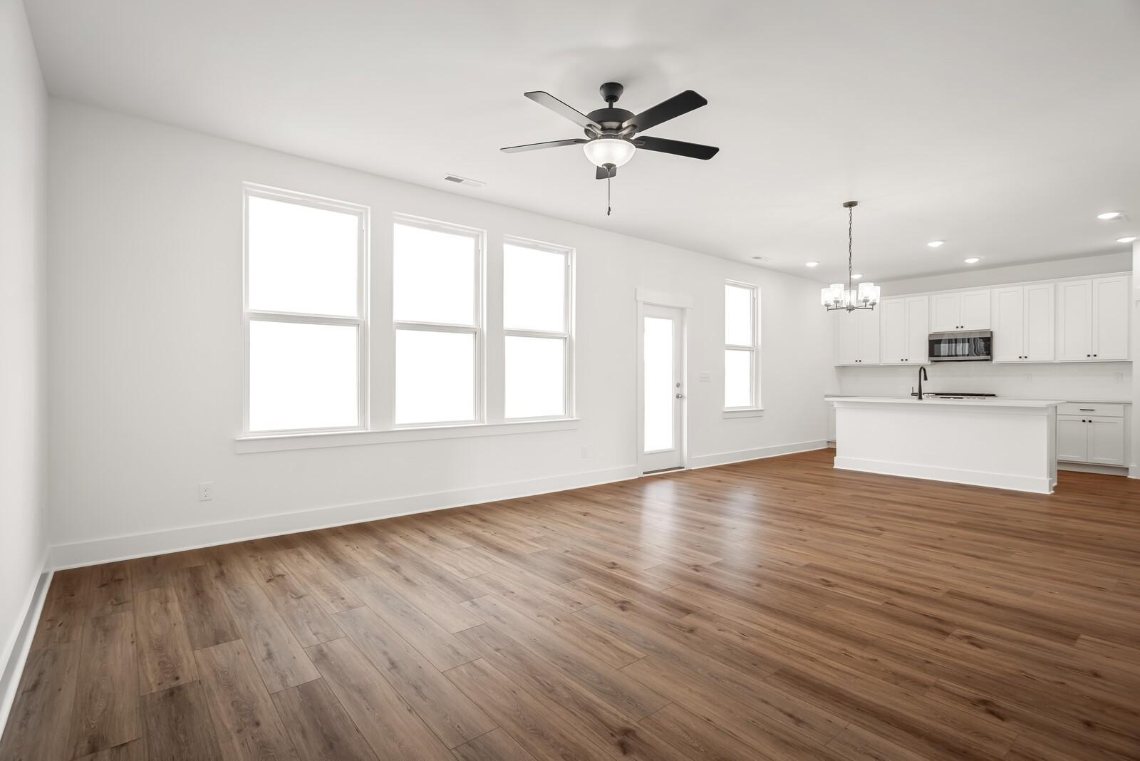 Open-concept kitchen with white cabinets, large island, ceiling fan, and hardwood floors in The Logan C by Davidson Homes, Gallatin, TN