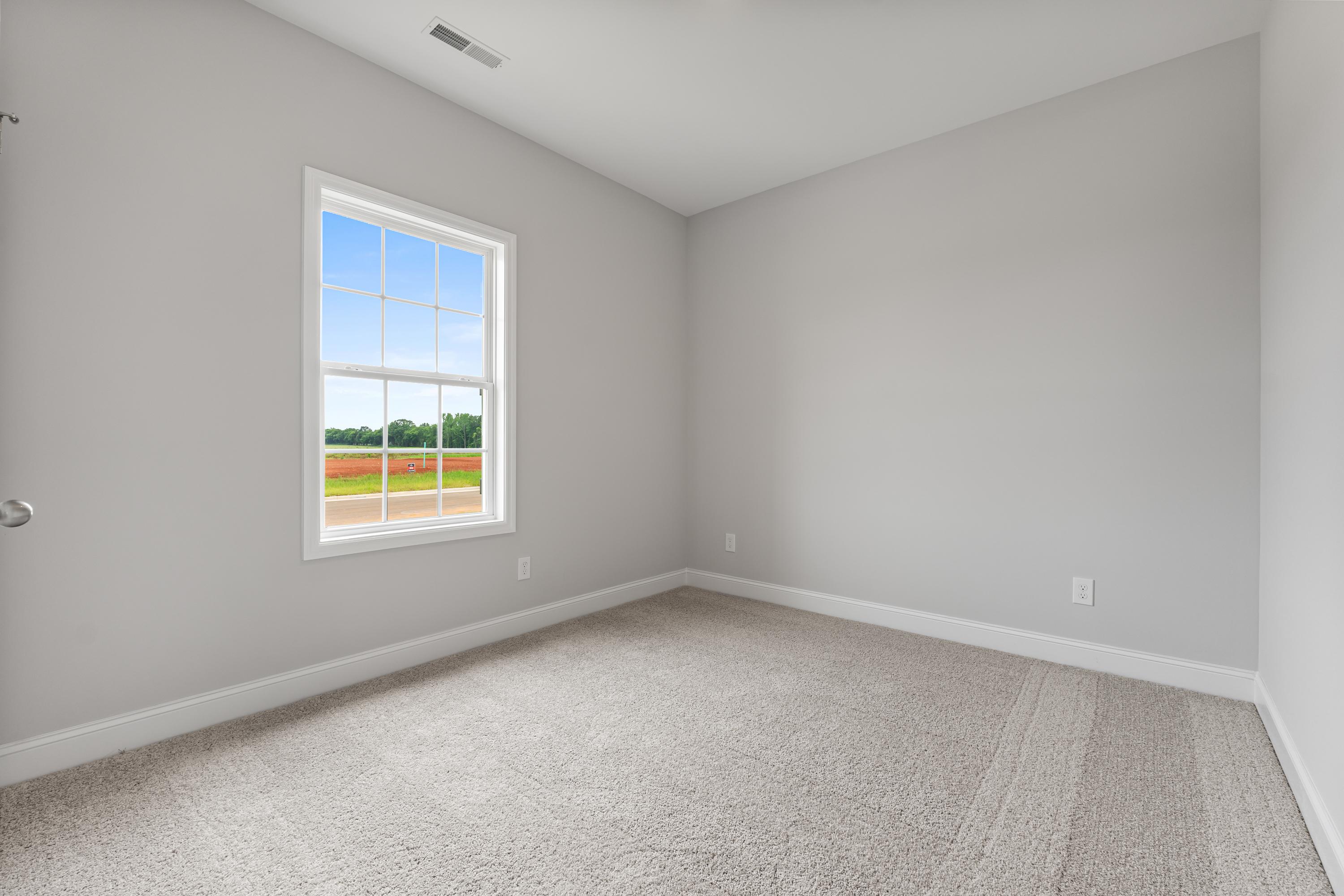 Spacious empty bedroom in The Butler by Davidson Homes, gray walls, carpet floor, large window with Alabama field view