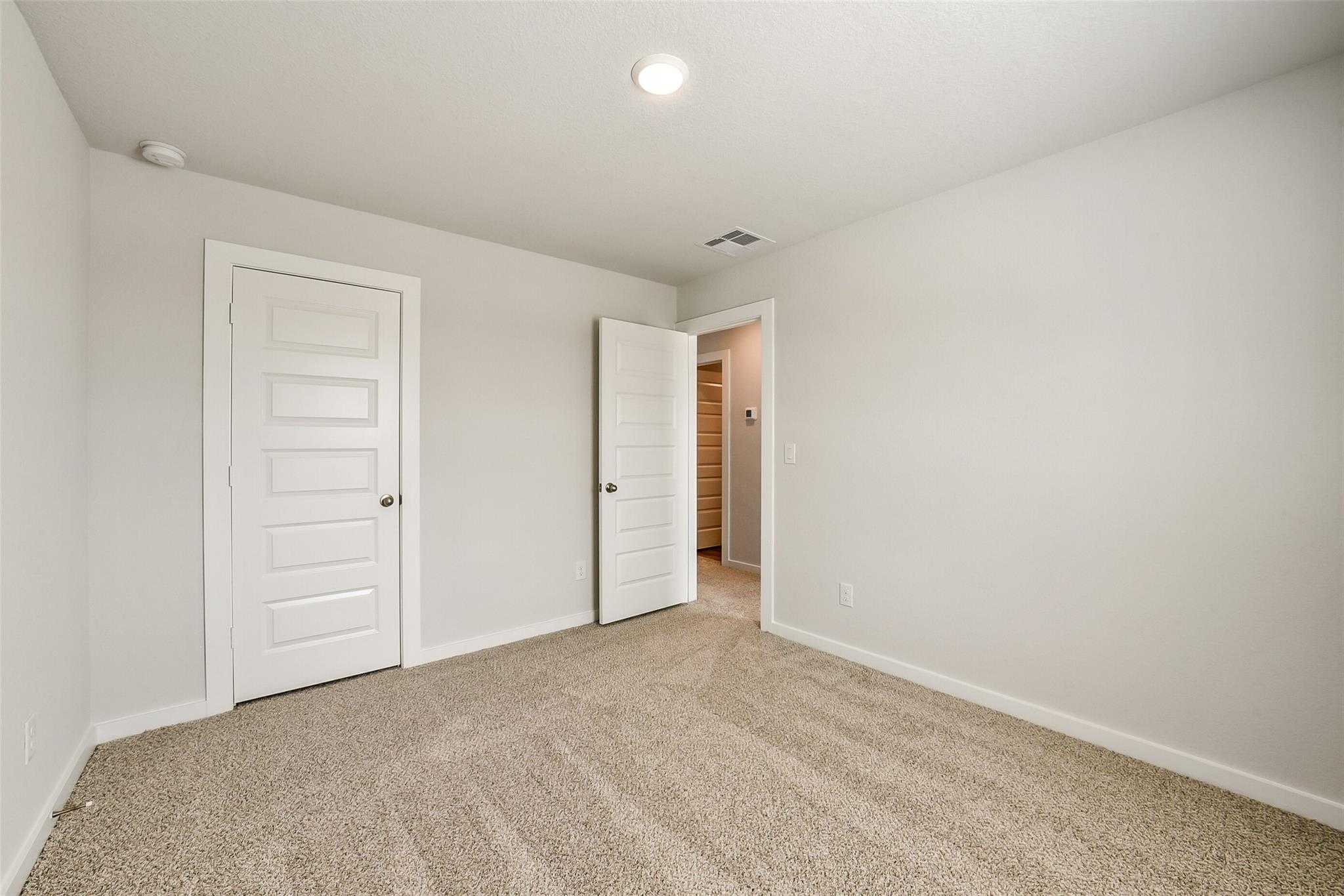Spacious secondary bedroom with double-door closet, beige carpet, and white walls in Davidson Homes The Trinity F, Magnolia, Texas