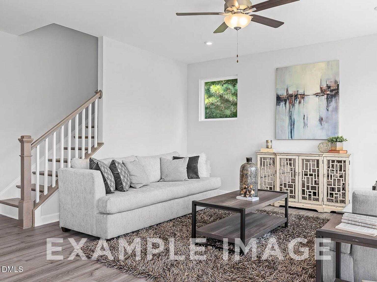 Cozy living room with gray sofa, wooden coffee table, area rug, ceiling fan, and staircase in Davidson Homes The Chestnut B, Lillington, NC